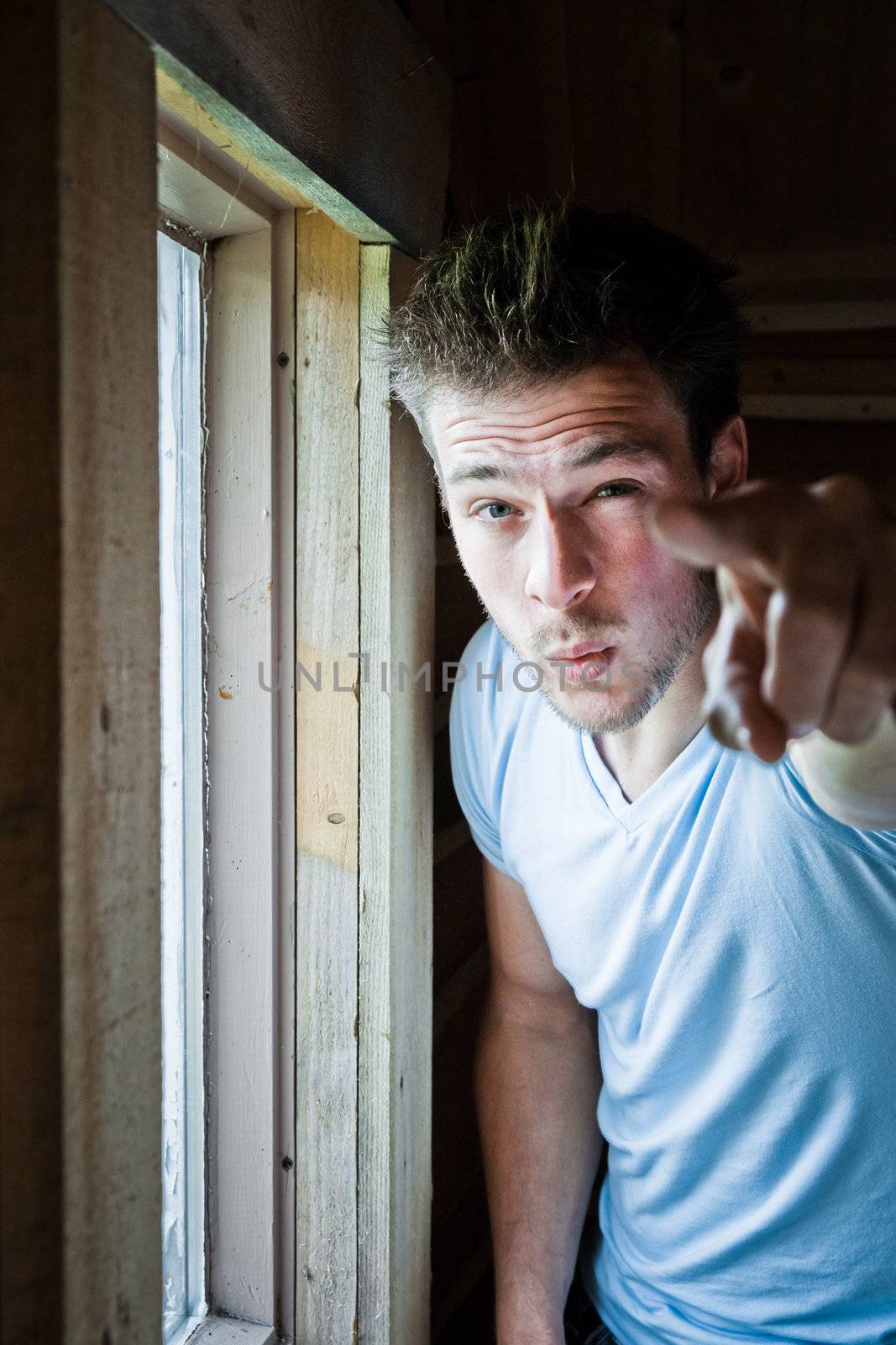 Young man at the window pointing at the camera