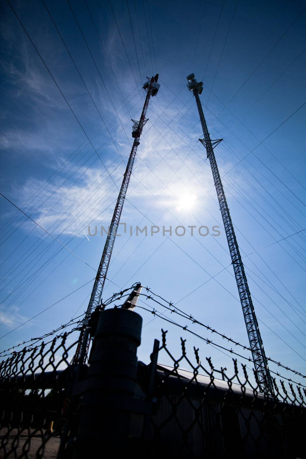 Pole with electrical wires and communication tower surounded by a fence