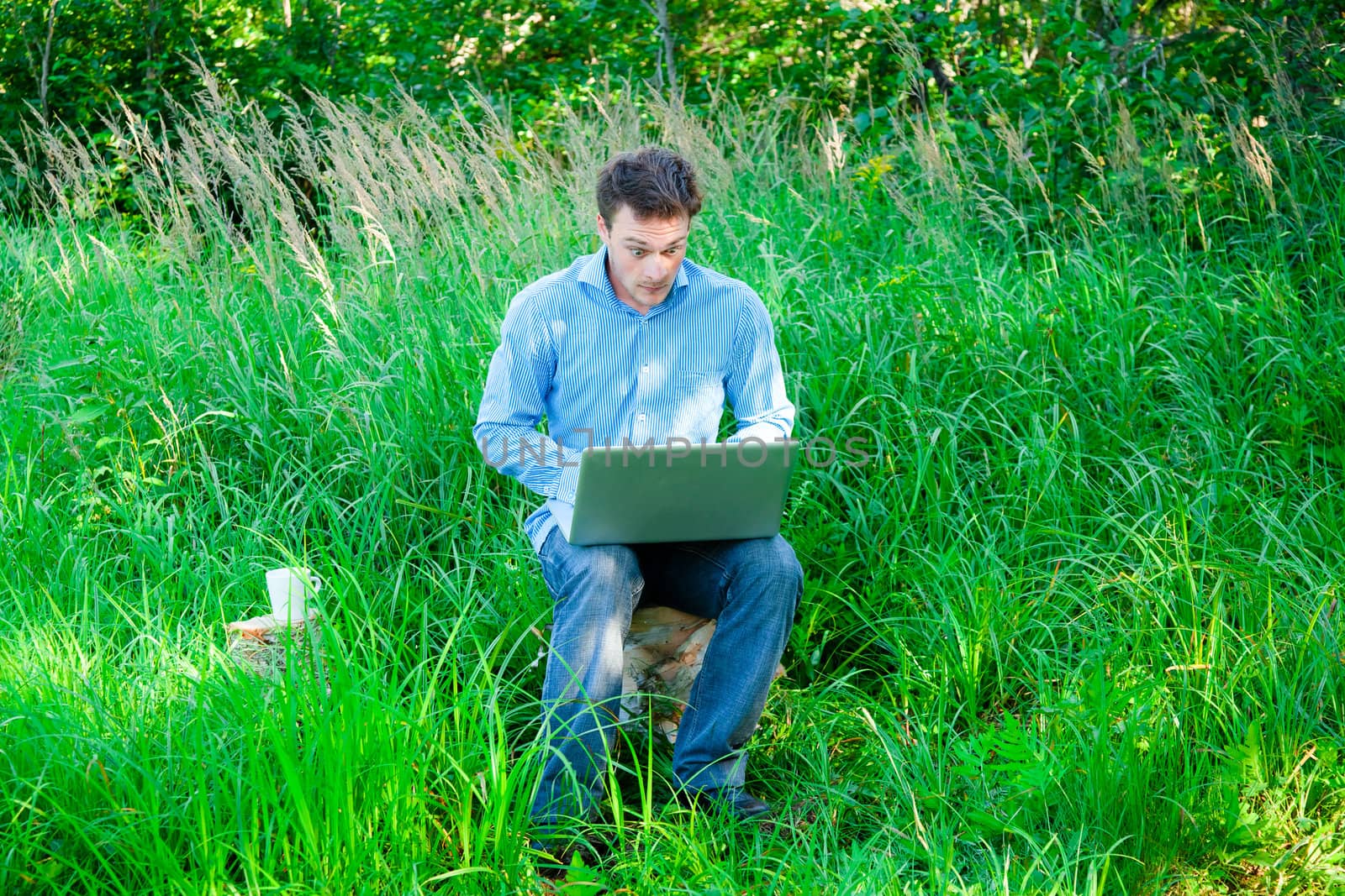 Surprised Young man outdoors with a cup and laptop in nature