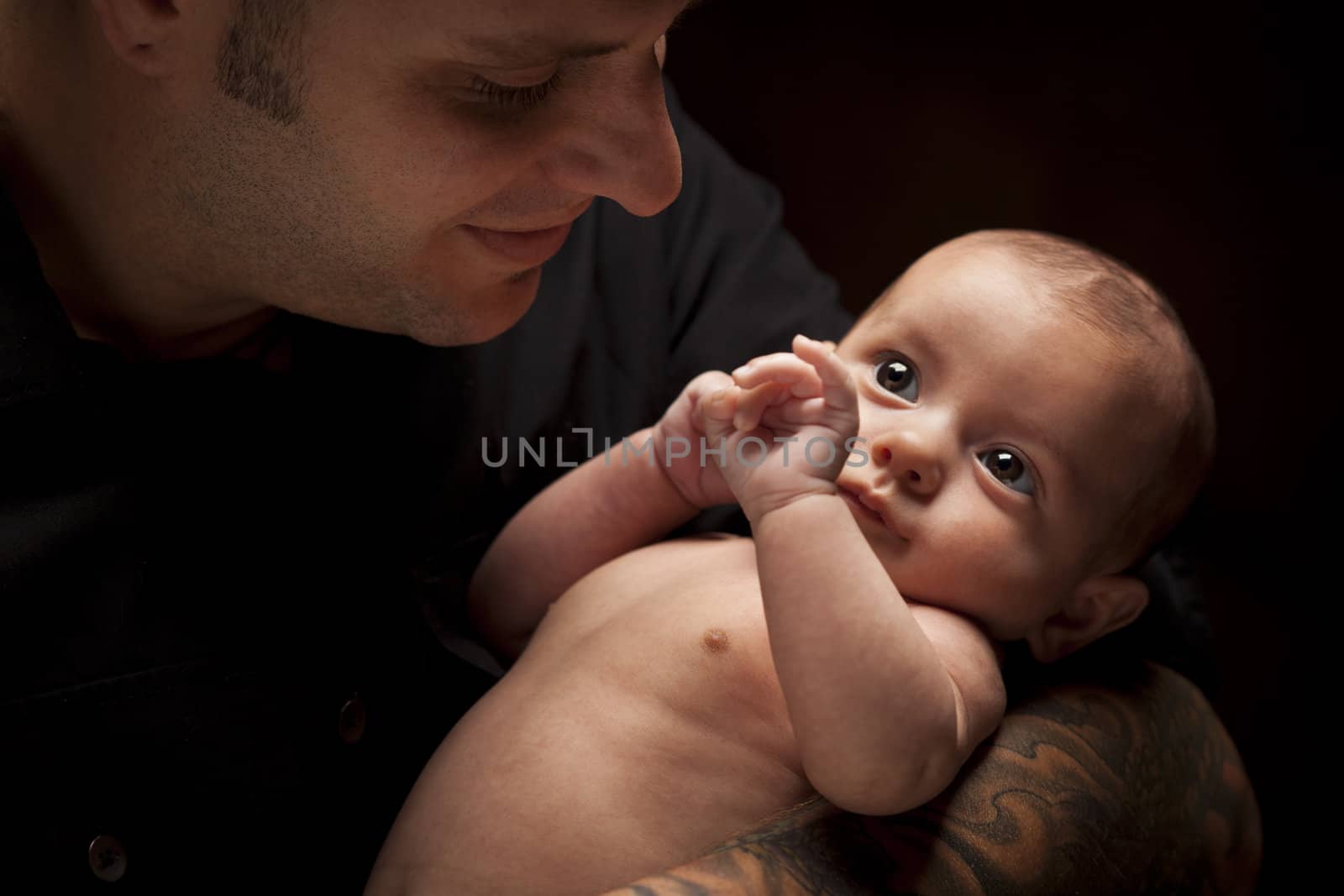 Happy Young Father Holding His Mixed Race Newborn Baby Under Dramatic Lighting.