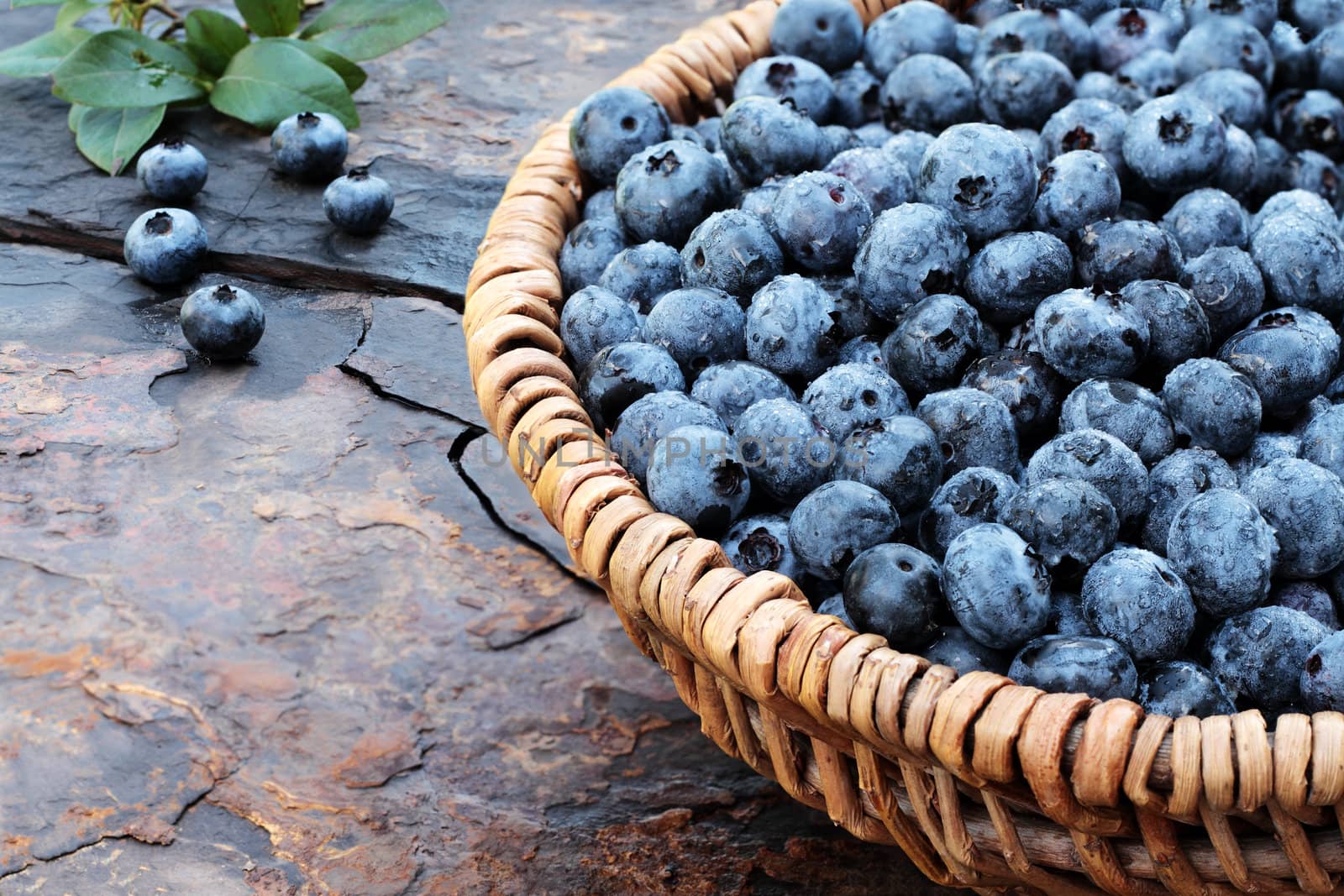 Fresh picked organic blueberries  in a woven basket on a rustic slate background. Shallow depth of field.