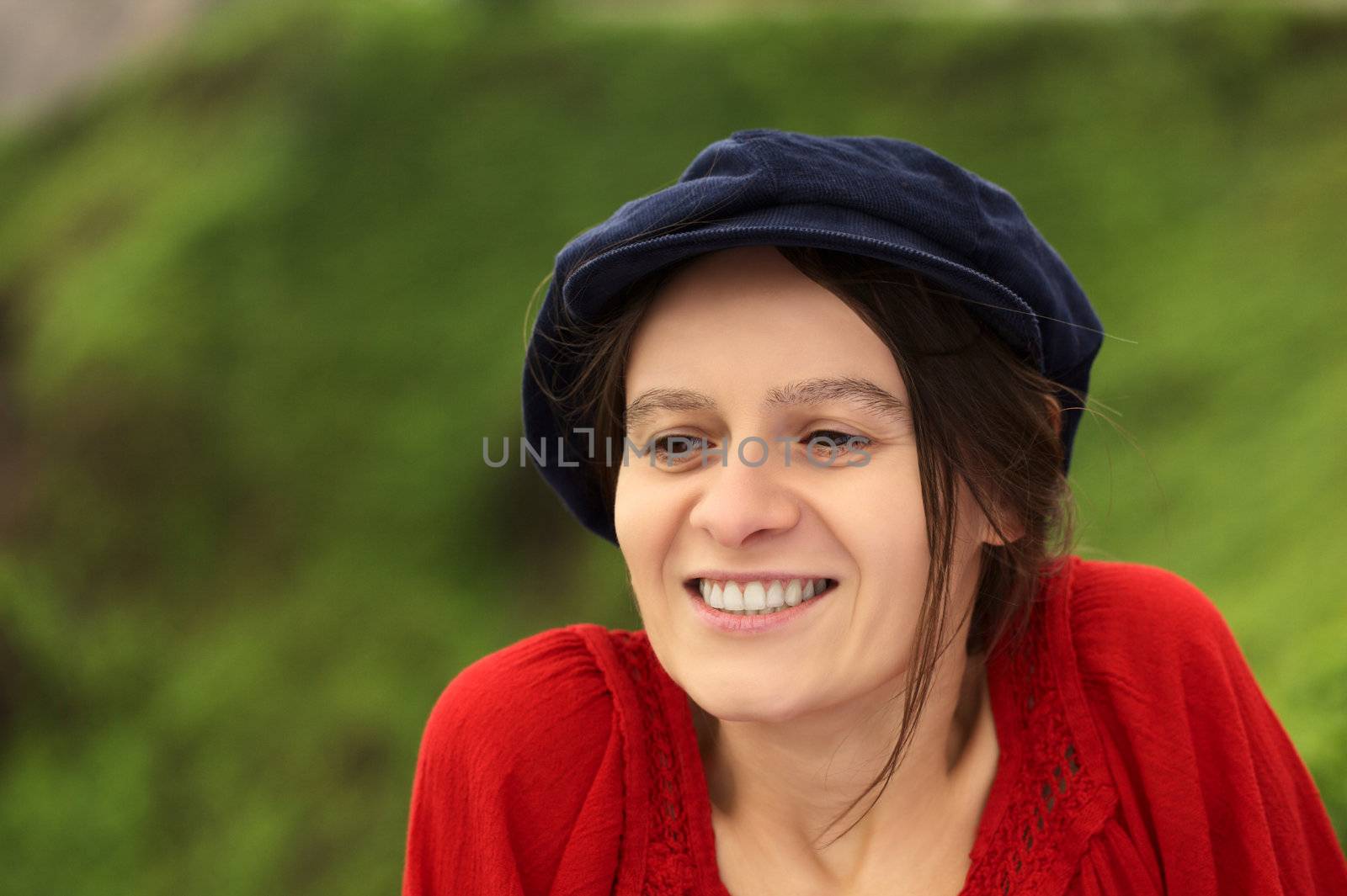 Smiling young Caucasian woman with a blue gatsby cap in a park (Selective Focus, Focus on the left eye)