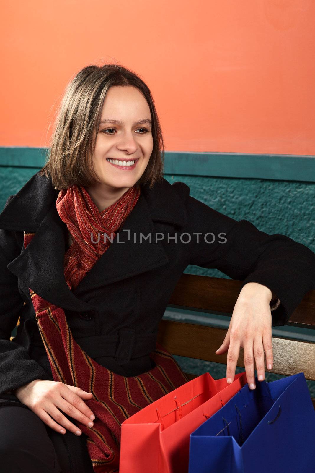 Happy young Caucasian woman with shopping bags sitting on a bench (Selective Focus, Focus on the right eye)