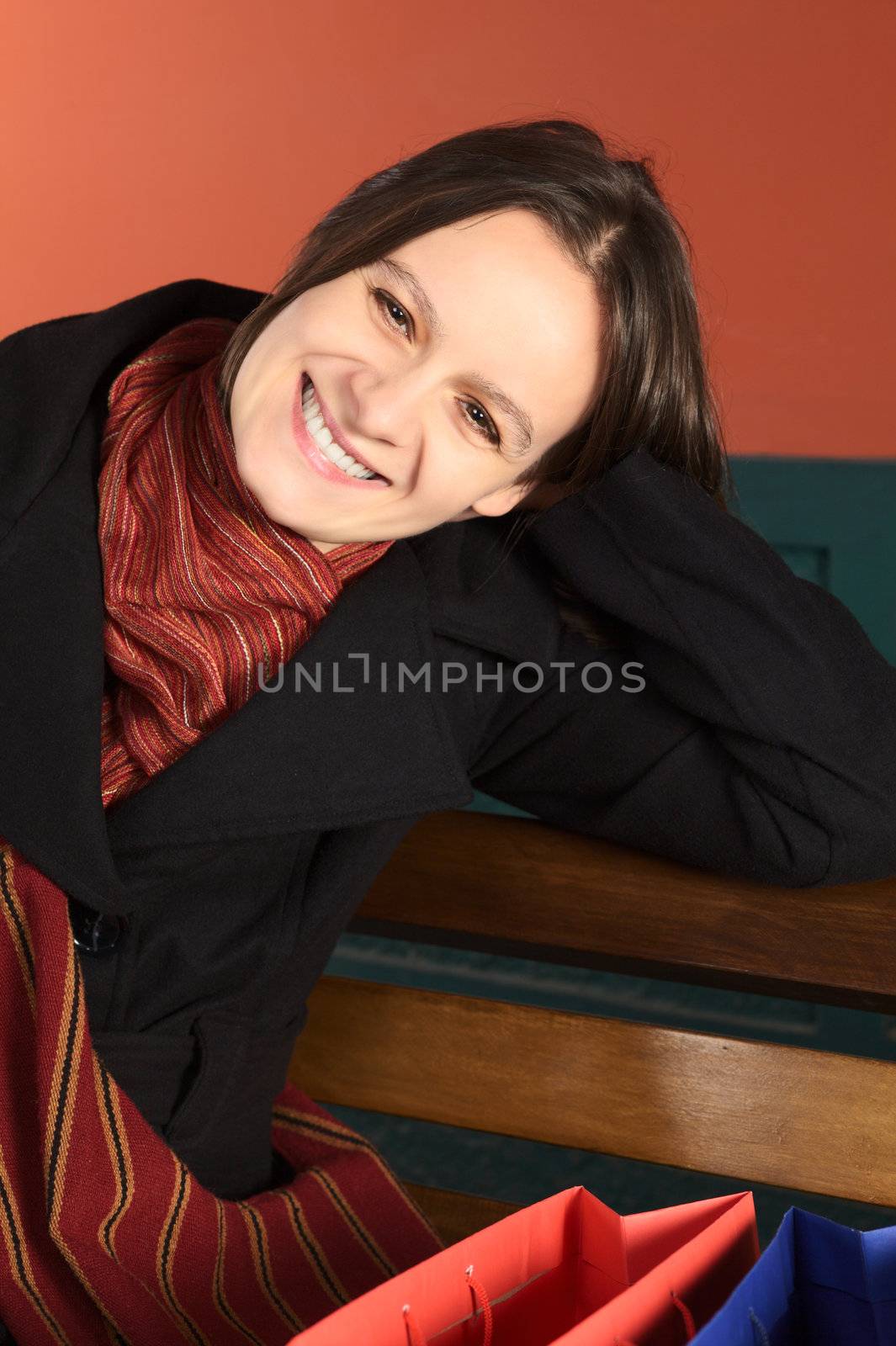Happy young Caucasian woman with shopping bags sitting on a bench (Selective Focus, Focus on the face)