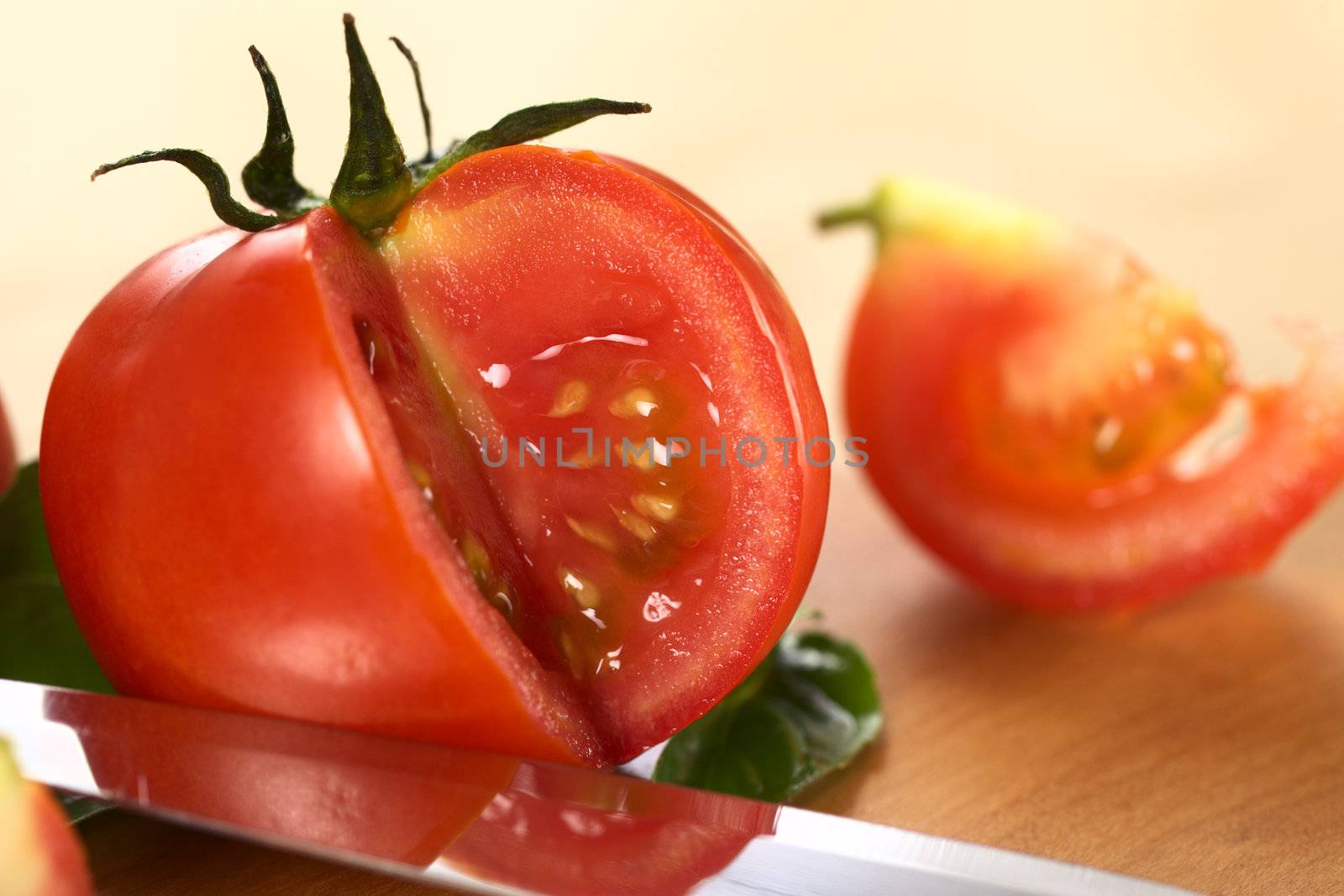 Globe tomato cut open on wooden board with a knife blade laying in front (Selective Focus, Focus on the seeds of the tomato)