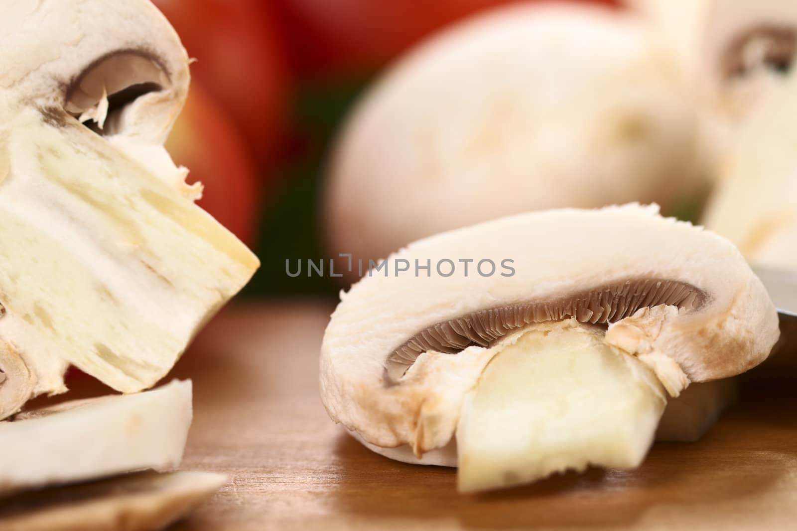 White mushroom slice with tomato and mushrooms in the back (Very Shallow Depth of Field, Focus on the gills of the mushroom slice)