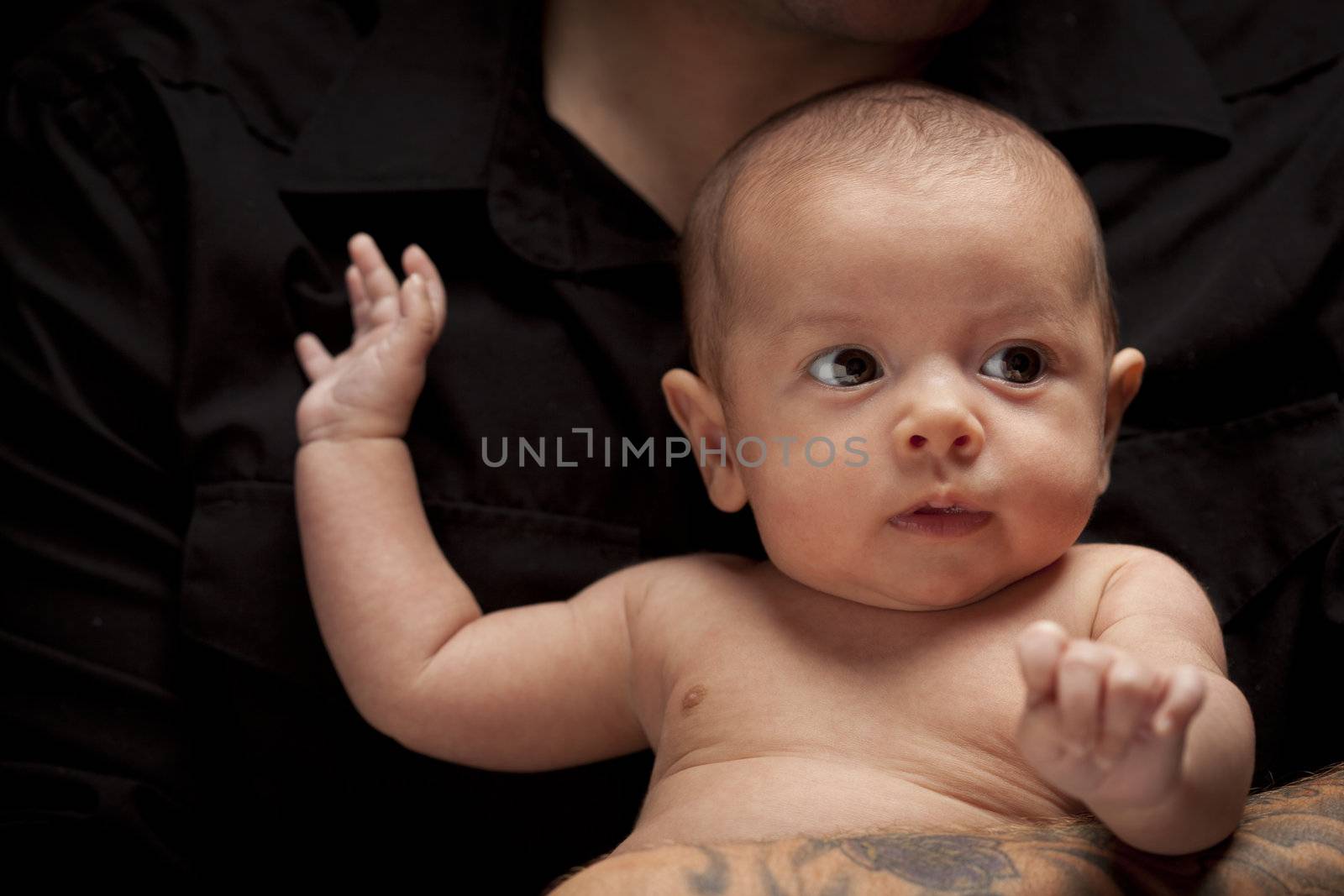 Young Father with Tattoo Holding His Mixed Race Newborn Baby Under Dramatic Lighting.
