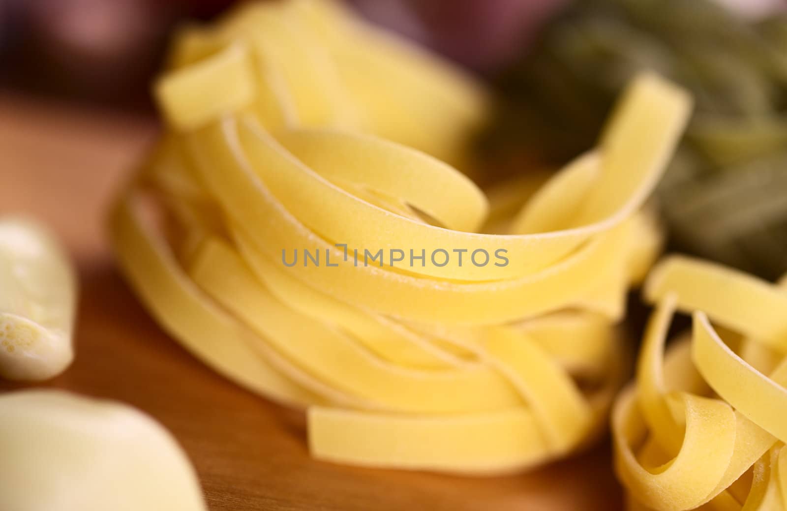 Raw Tagliatelle pasta surrounded by garlic (Very Shallow Depth of Field, Focus on the upper rim of the upper tagliatelle)