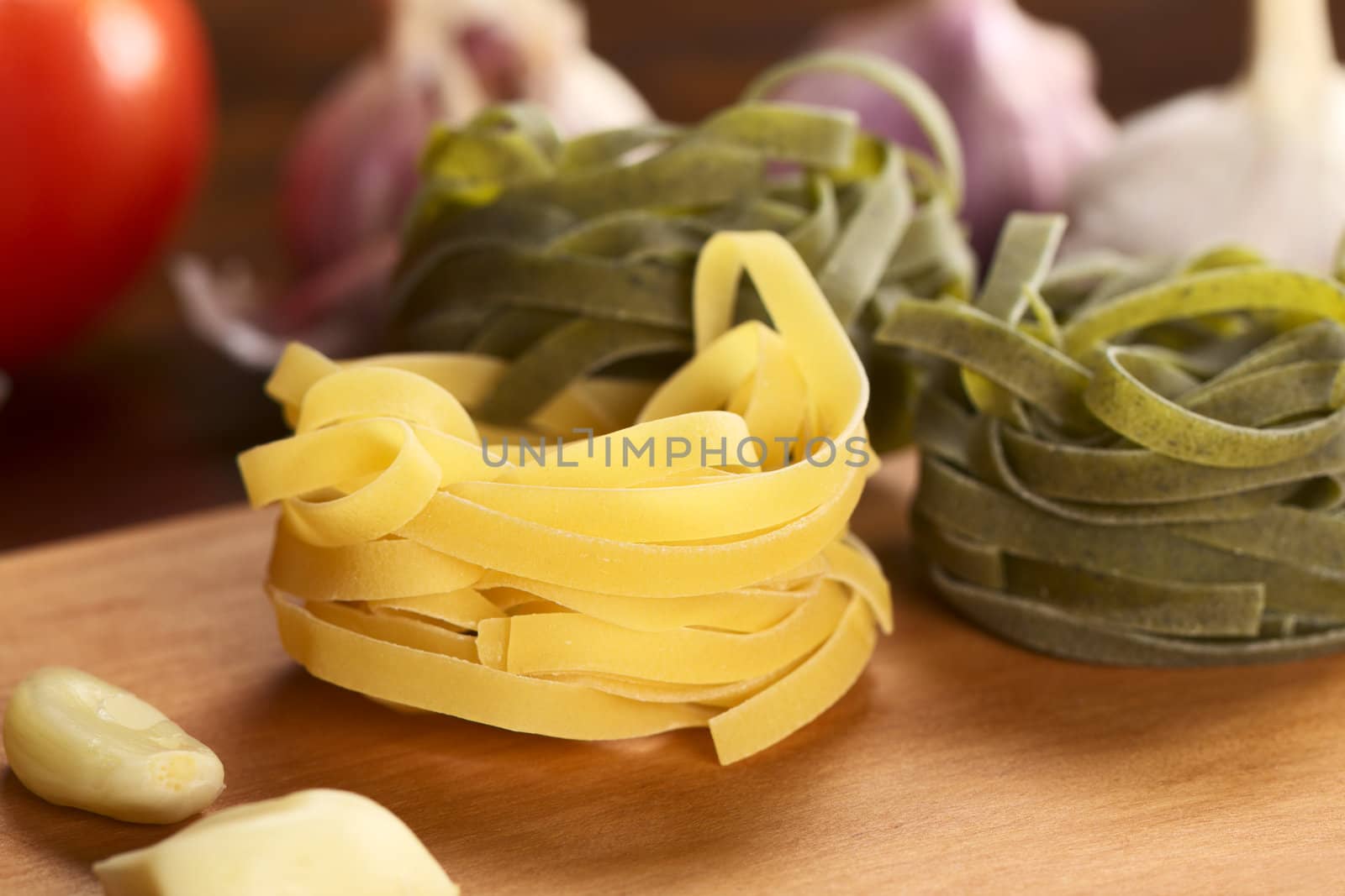 Raw tagliatelle paglia e fieno (straw and hay). Plain yellow pasta and with spinach flavored green pasta surrounded by garlic and tomato (Selective Focus, Focus on the front of the upper yellow tagliatelle strips) 