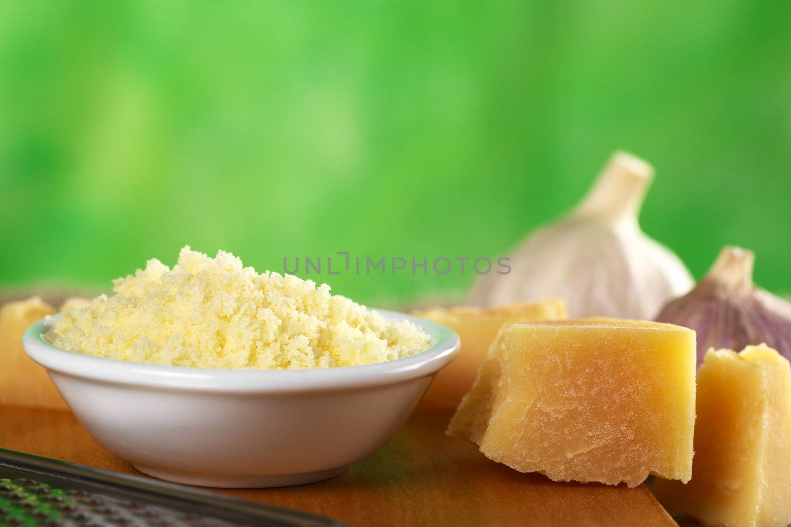 Grated Italian hard cheese with a piece of cheese beside (Selective Focus, Focus on the top of the grated cheese pile and the front upper edge of the cheese piece beside)
