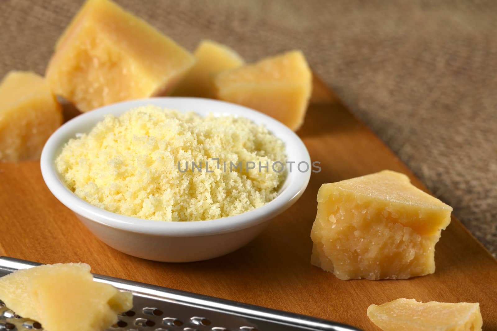 Grated Italian hard cheese with hard cheese pieces around (Selective Focus, Focus on the top of the grated cheese)