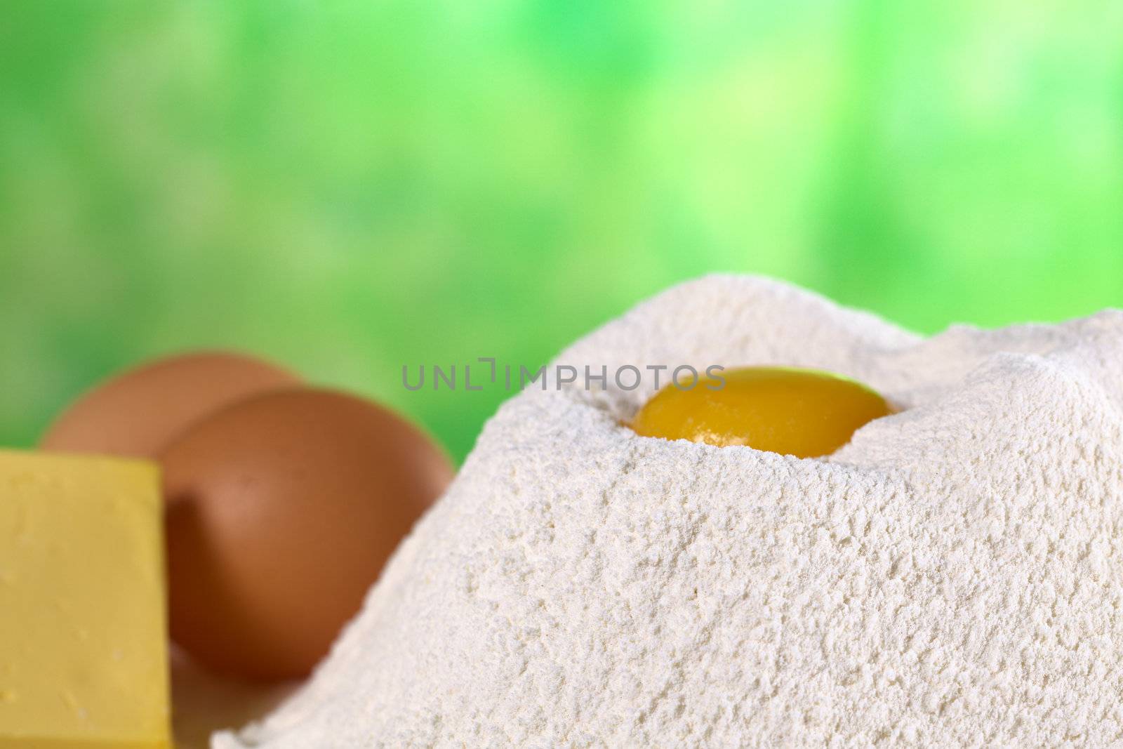 Flour with egg yolk in the middle surrounded with butter and eggs on the side (Selective Focus, Focus on the upper front edge of the flour pile)
