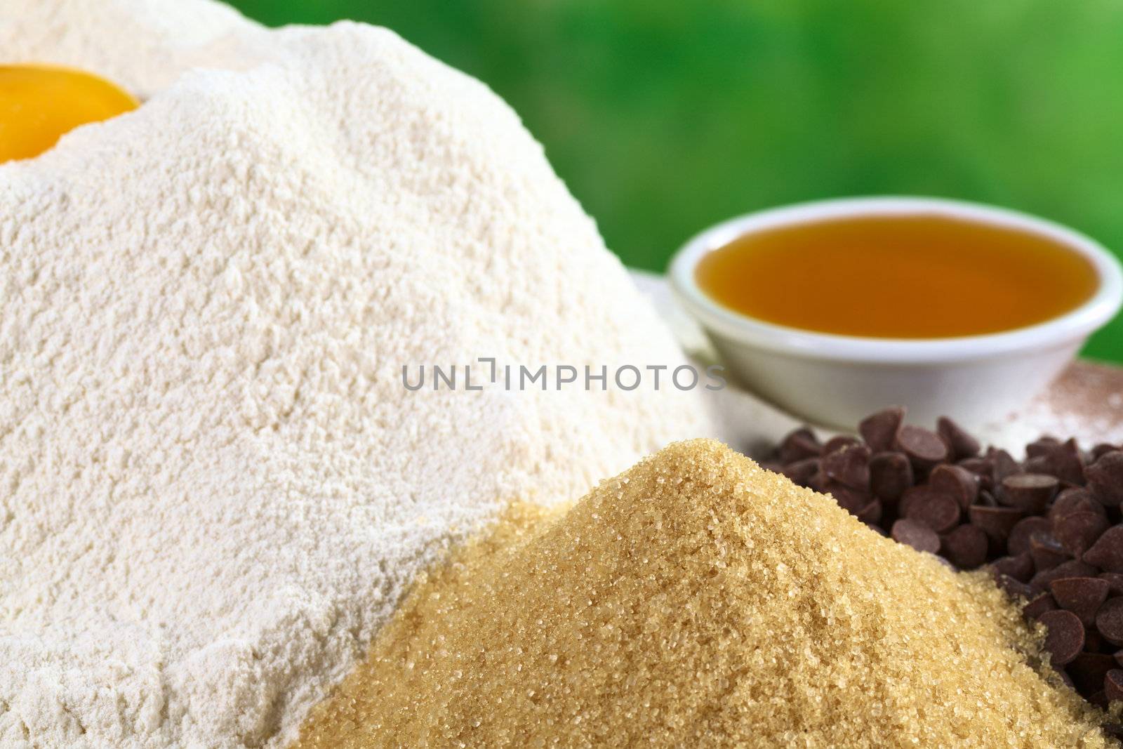Granulated brown sugar with white flour, chocolate chips and honey in the back (Selective Focus, Focus on the top of the sugar pile)
