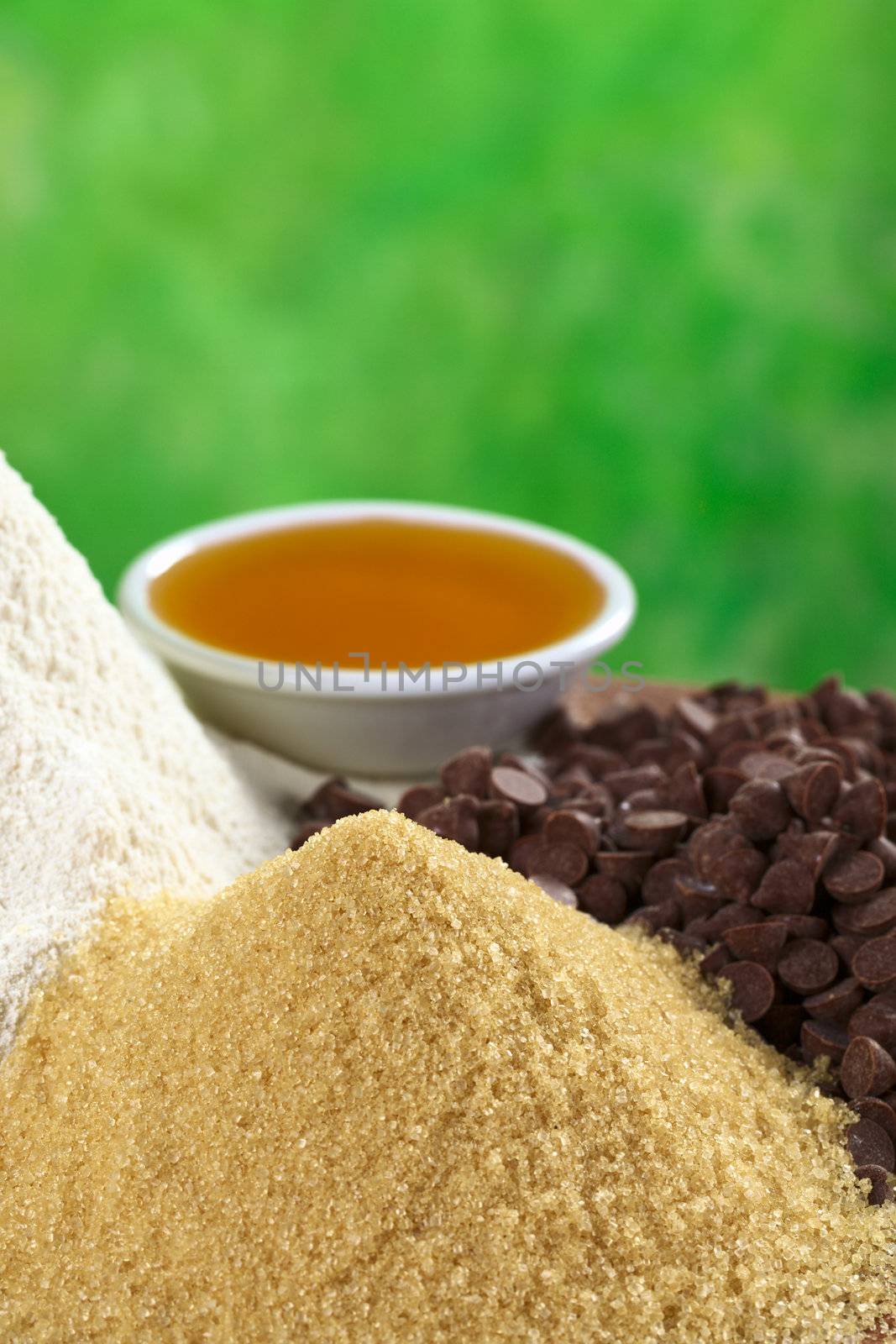 Granulated brown sugar with white flour, chocolate chips and honey in the back (Selective Focus, Focus on the top of the sugar pile)