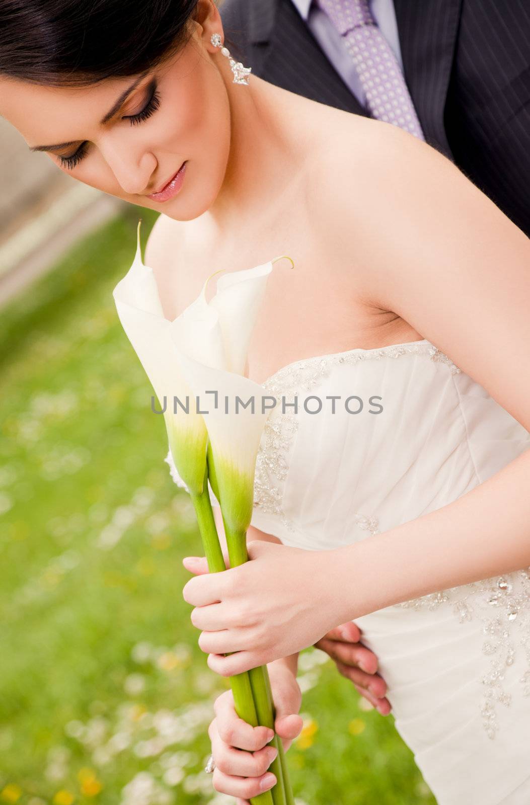 Beautiful bride holding white callas groom behind hidden
