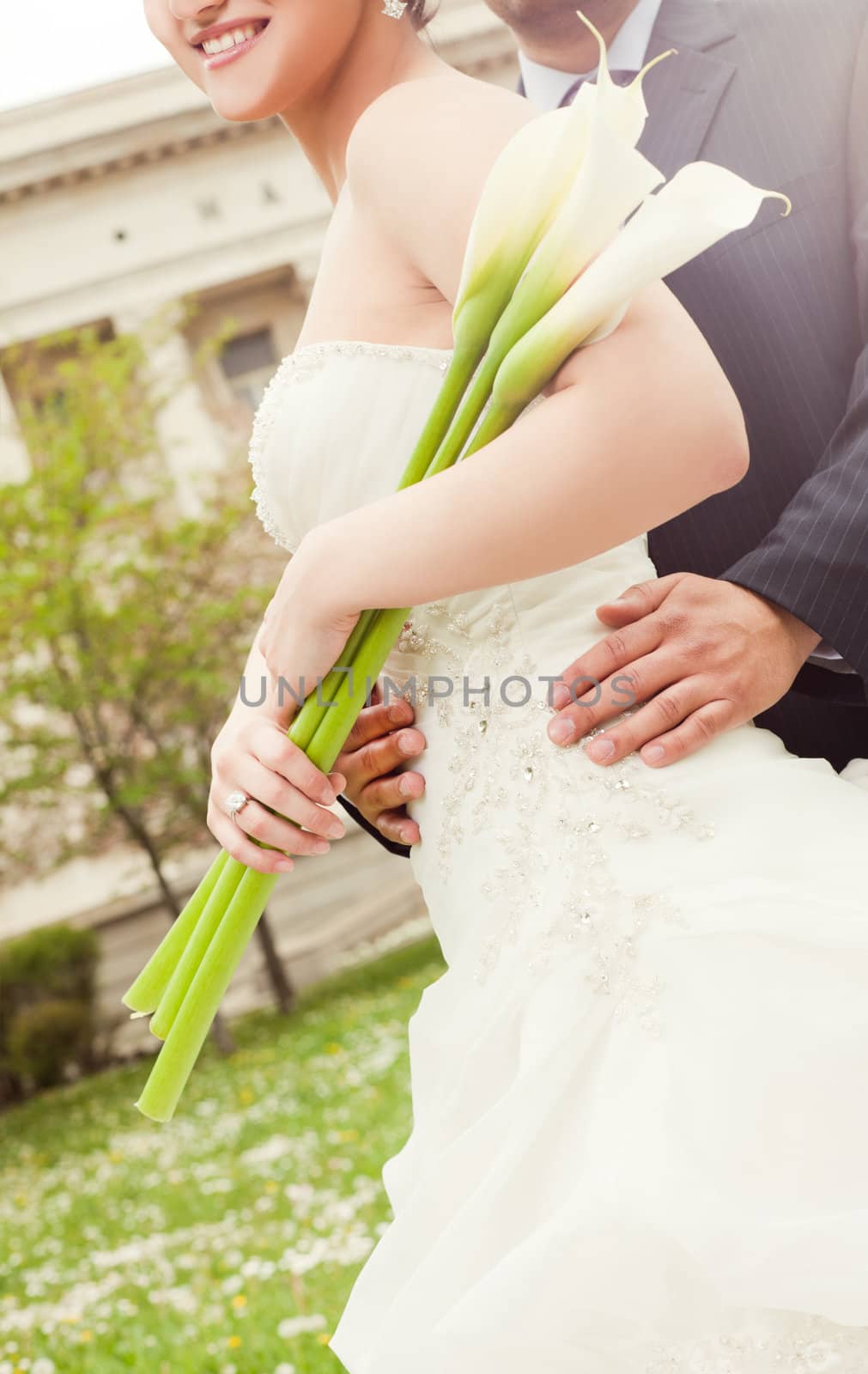 Cropped image of wedding couple embracing, woman holding white calla lilies