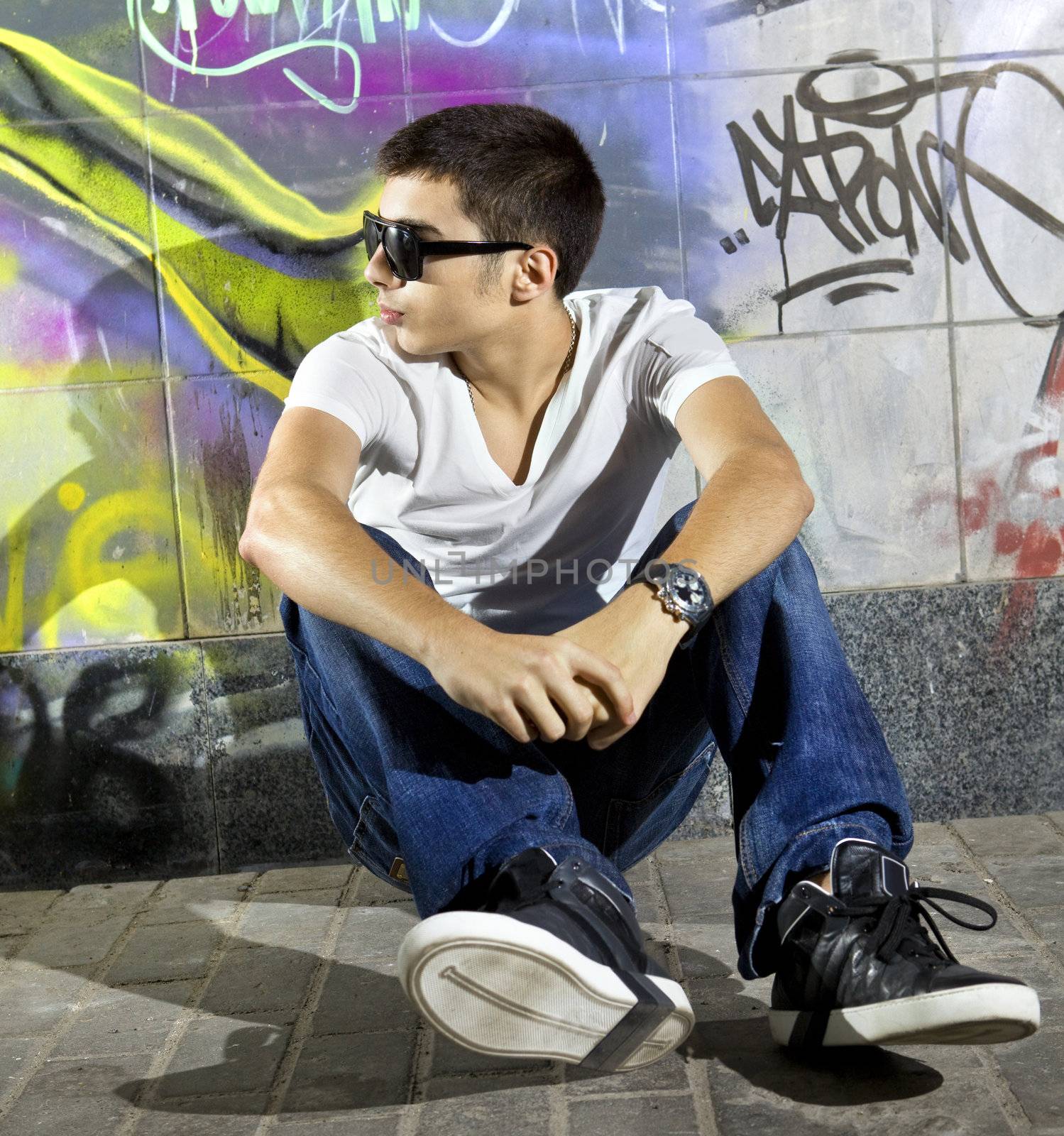 young man sitting in front of a colorful graffiti wall