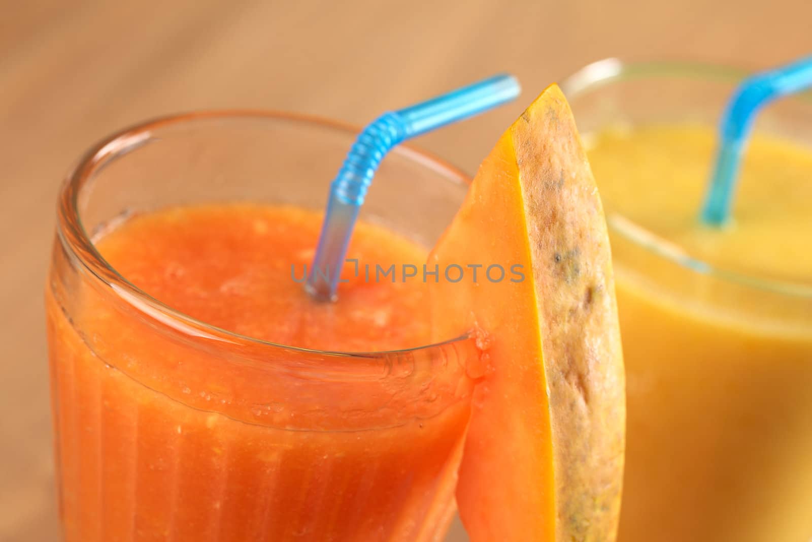 Fresh papaya juice garnished with a papaya slice, mango juice in the back (Selective Focus, Focus on the upper edge of the papaya slice and the front rim of the glass)