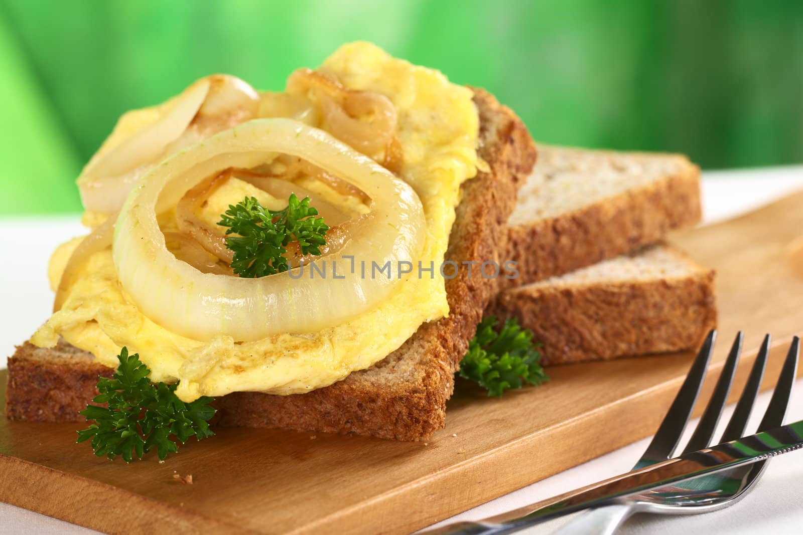 Scrambled eggs open sandwich with fried onions and fresh parsley leaves (Selective Focus, Focus on the front of the onion and the parsley on top)