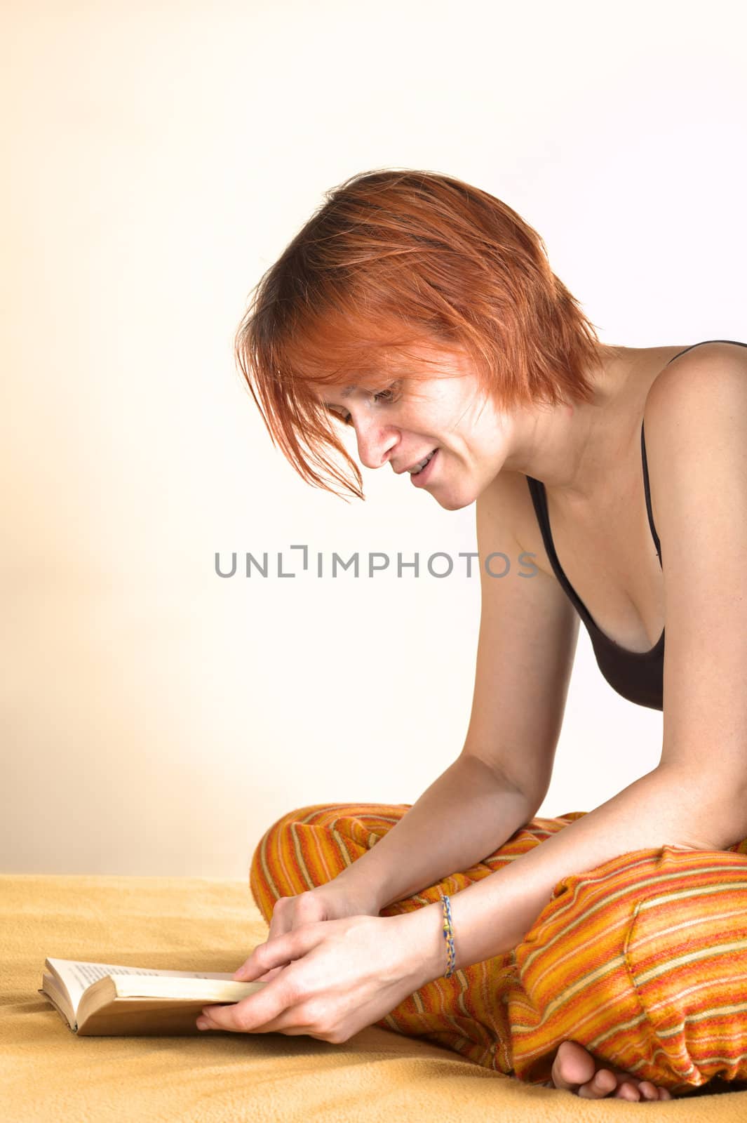 Young woman sitting cross-legged on bed and reading a book (Selective Focus, Focus on the face of the woman)