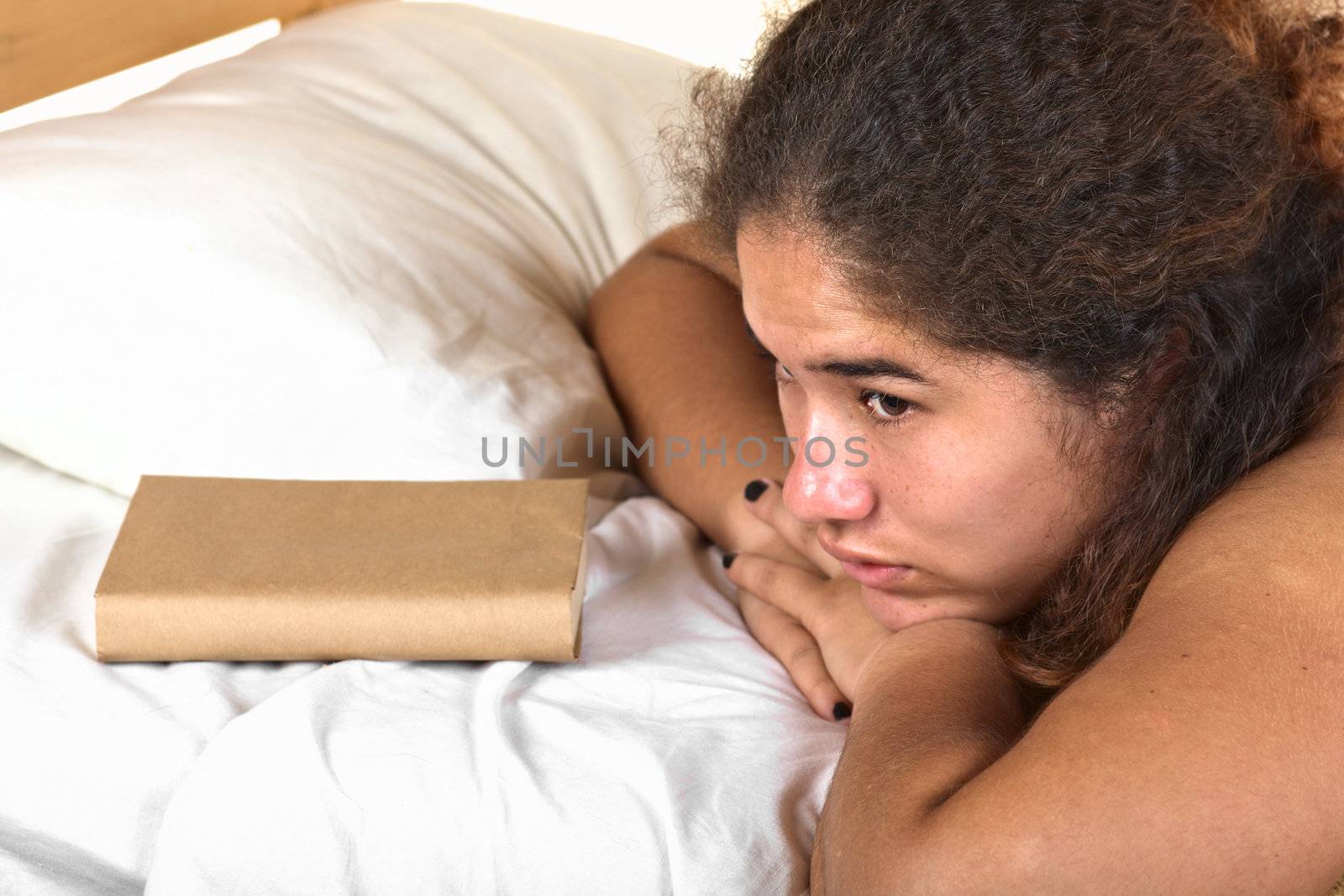 Young Peruvian woman resting on bed with a book in front of her (Selective Focus, Focus on the left eye of the woman)