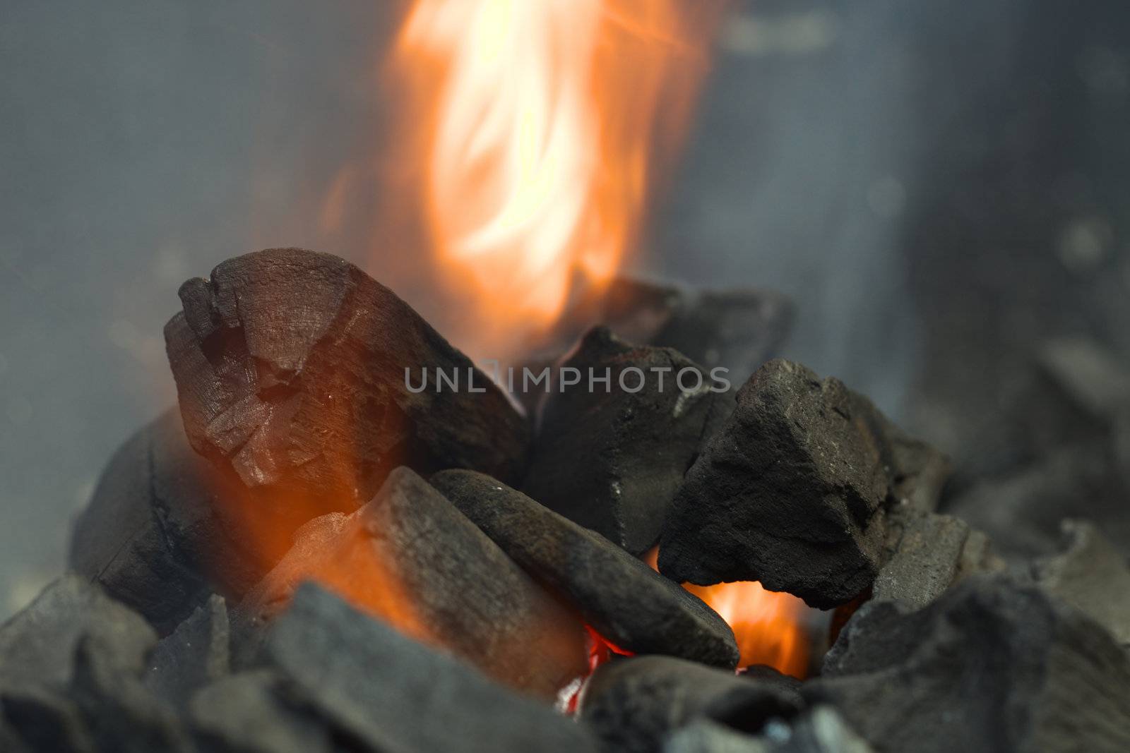 Burning charcoal with orange-colored flame and smoke (Selective Focus, Focus on the front of the big charcoal piece on the left side of the flame)