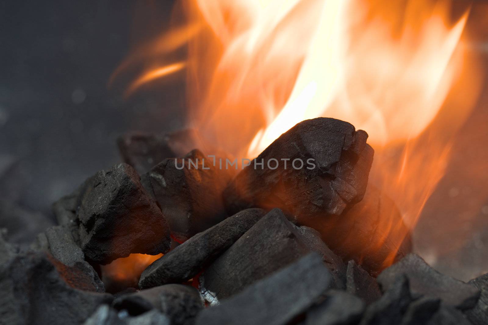 Burning charcoal with orange-colored flame and smoke (Selective Focus, Focus on the front of the big charcoal piece in the middle of the flame)