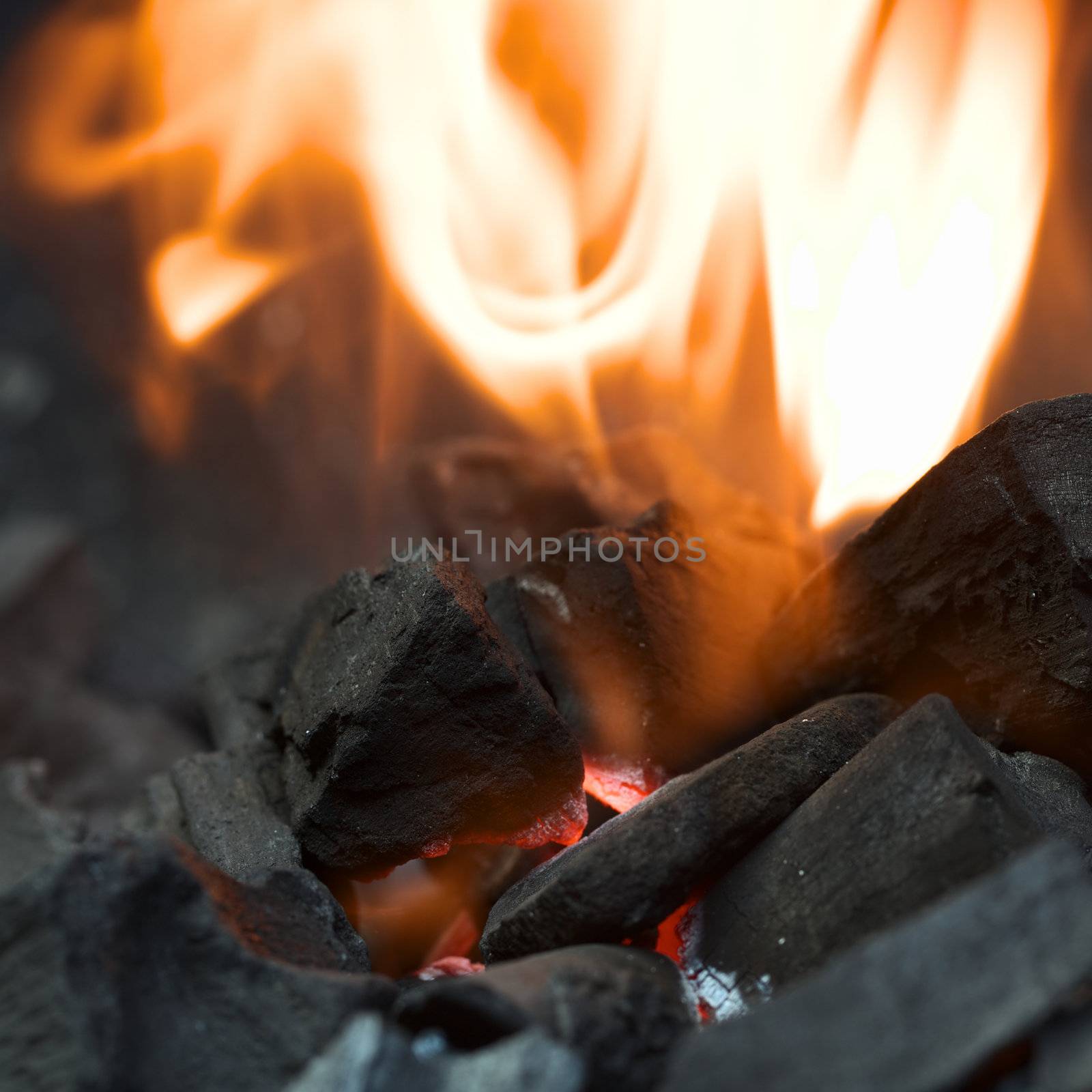 Burning charcoal with orange-colored flame and glow (Selective Focus, Focus on the front of the charcoal piece on the left side of the flame)