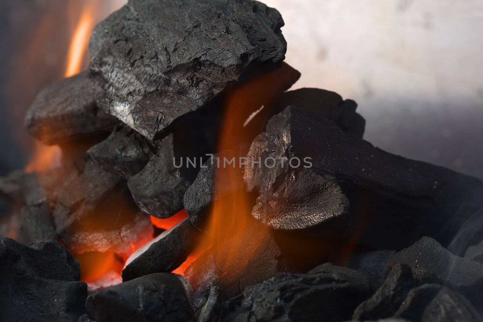Burning charcoal with orange-colored flame and glow (Selective Focus, Focus on parts of the charcoal around the flame)