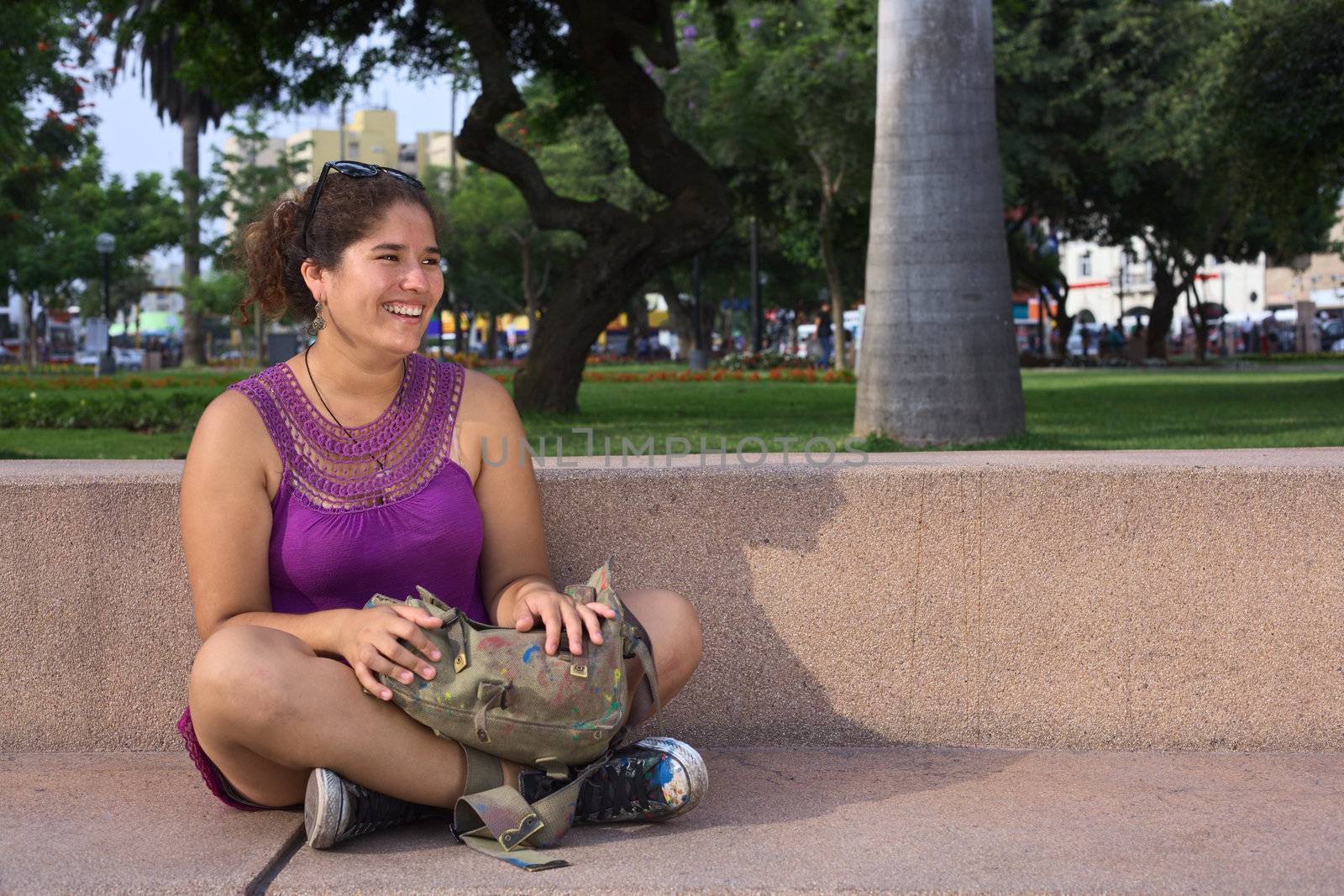 Beautiful smiling young Peruvian woman sitting cross-legged in a park in Lima, Peru (Selective Focus, Focus on the face of the woman)