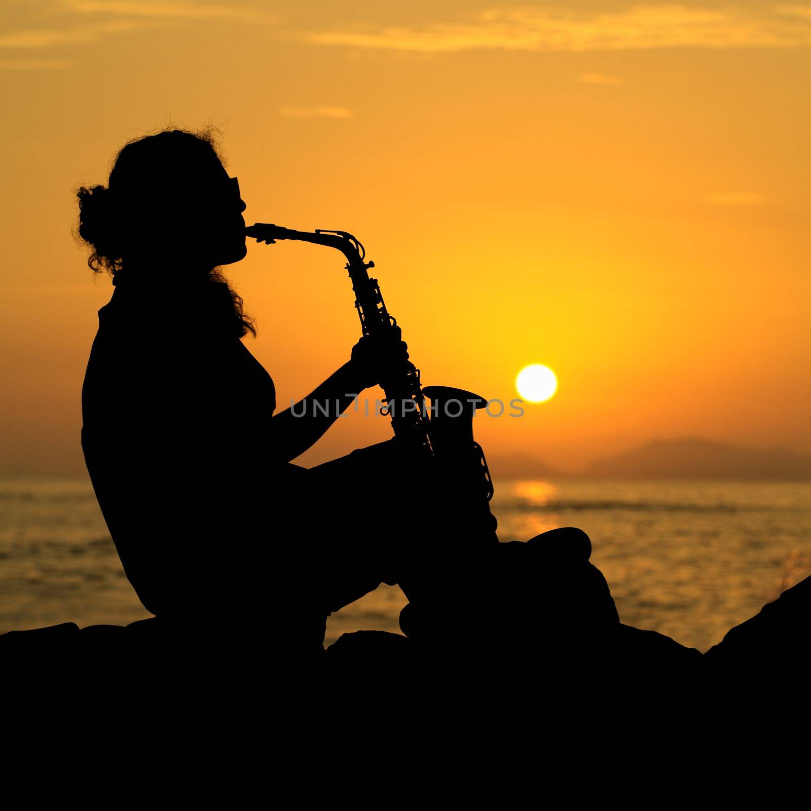 The silhouette of a young female musician playing her saxophone on the coast at sunset