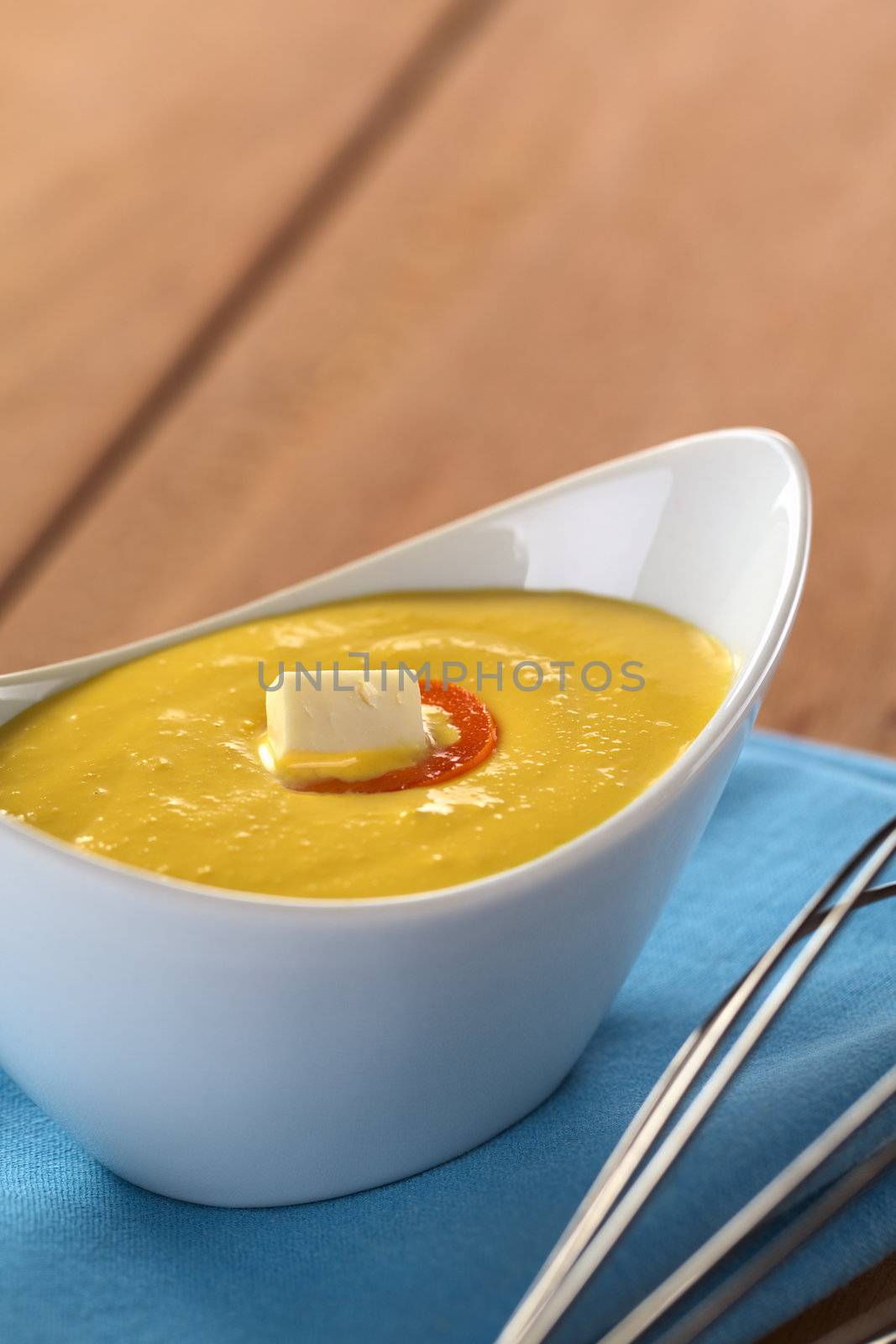 Peruvian Huancaina Sauce (spicy cheese sauce) made of cheese, soda crackers, aji (Peruvian yellow chili pepper) and milk in a ceramic bowl with beater on the side (Selective Focus, Focus on the front of the cheese on the sauce) 