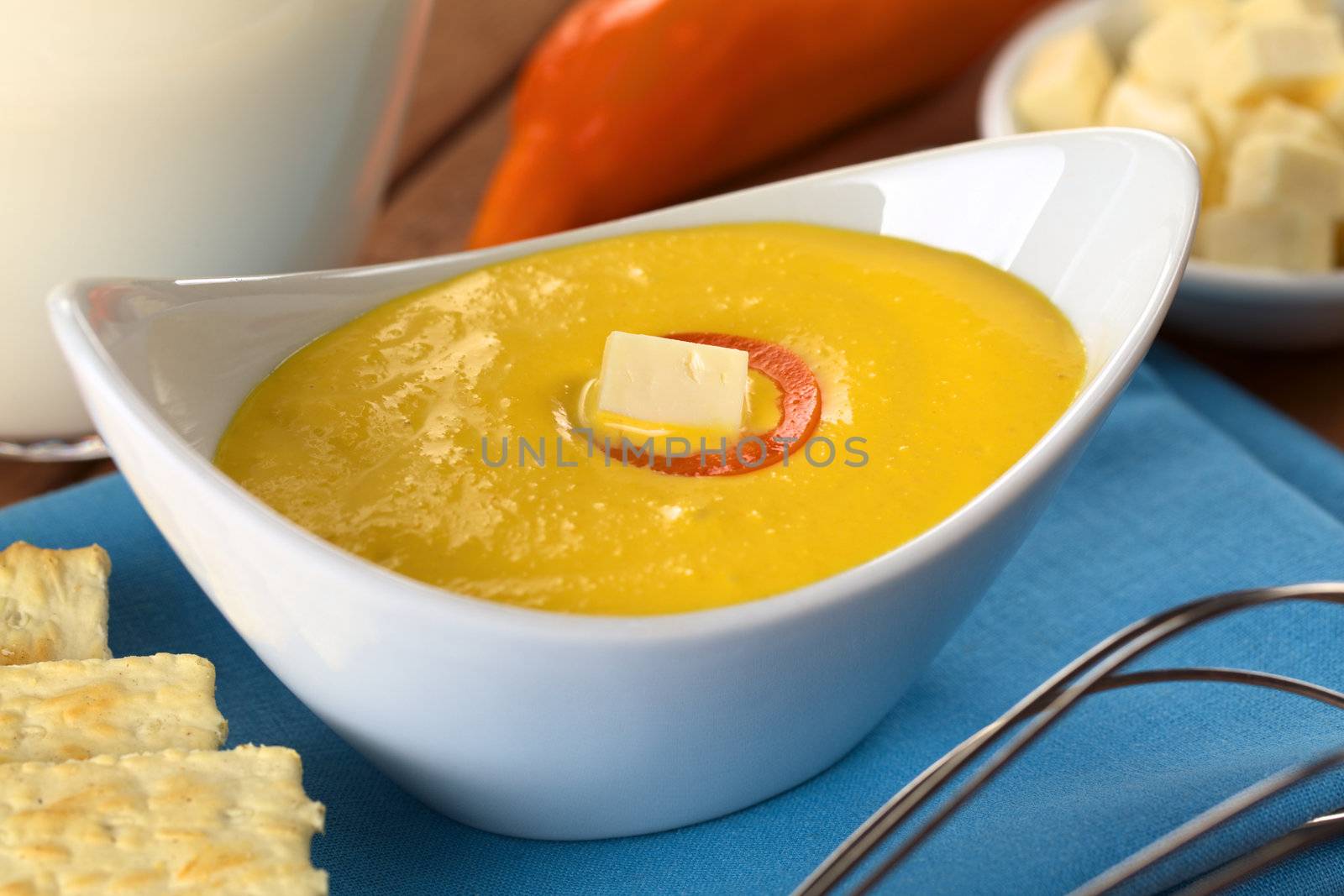 Peruvian Huancaina Sauce (spicy cheese sauce) in ceramic bowl surrounded by its ingredients: cheese, soda crackers, aji (Peruvian yellow chili pepper) and milk (Selective Focus, Focus on the front of the cheese on the sauce) 