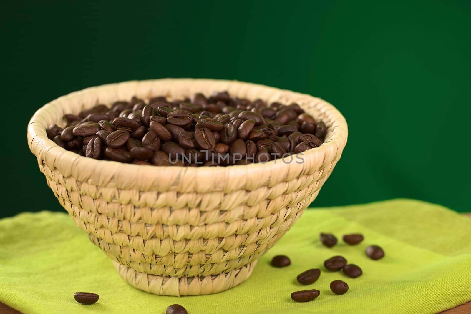 Roasted coffee beans in woven basket with green background (Selective Focus, Focus on the coffee beans in the middle of the basket)