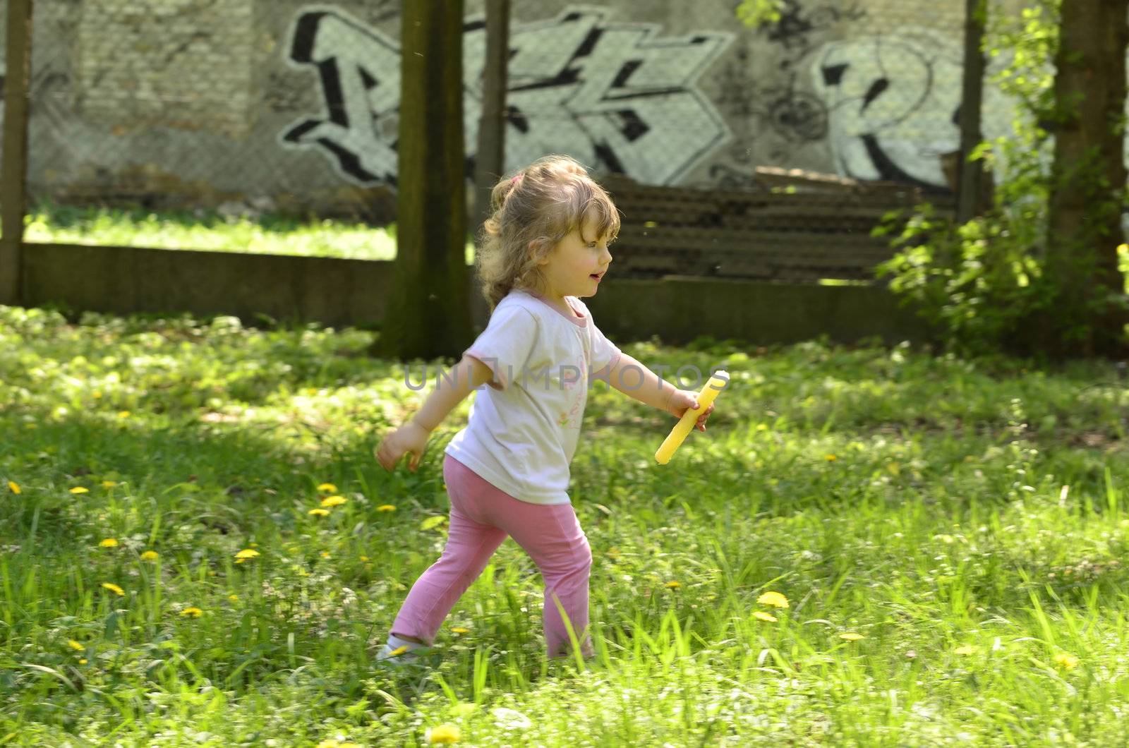 Photo shows a little girl with a rod of popcorn in hand, runs across the grass in the park.