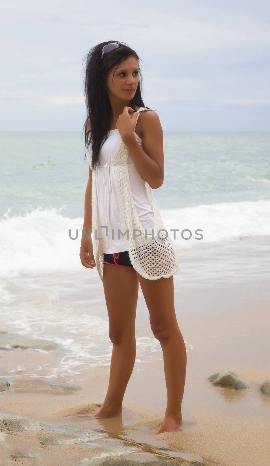 Slim brunette on a beach in a white dress against a background of sea waves