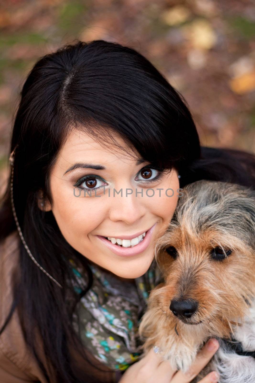 A young woman in her 20s by the sea shore holds a cute mixed breed beagle yorkshire terrier dog also called a Borkie.