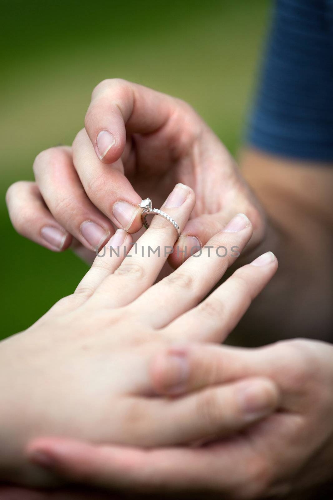 Man placing a diamond engagement ring on the finger of his fiance.  Shallow depth of field with focus on the ring.