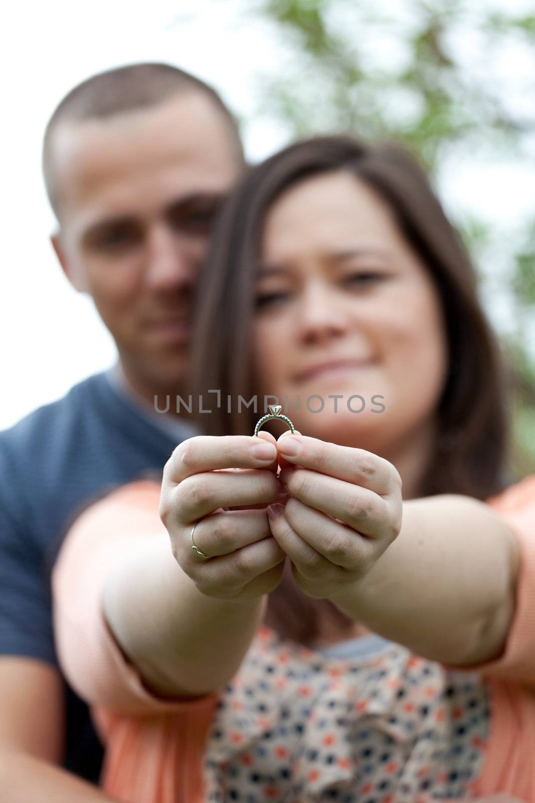 Young happy couple holding a diamond engagement ring.  Shallow depth of field with focus on the ring.