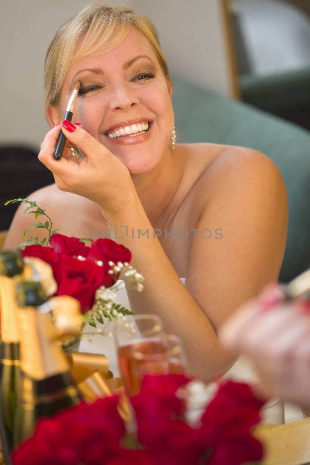 Attractive Blonde Woman Applies Her Makeup at a Mirror Near Champagne and Roses.