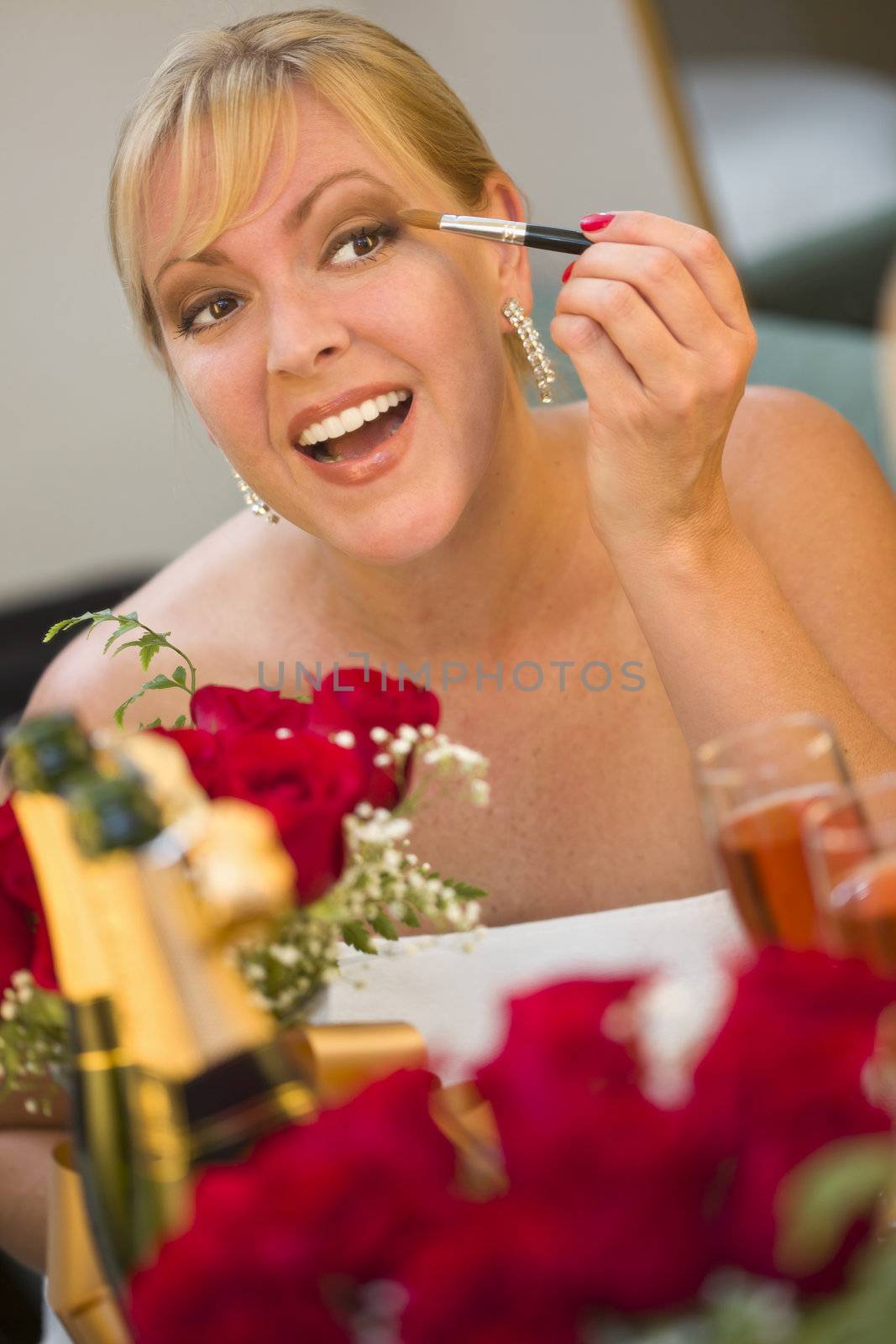 Attractive Blonde Woman Applies Her Makeup at a Mirror Near Champagne and Roses.