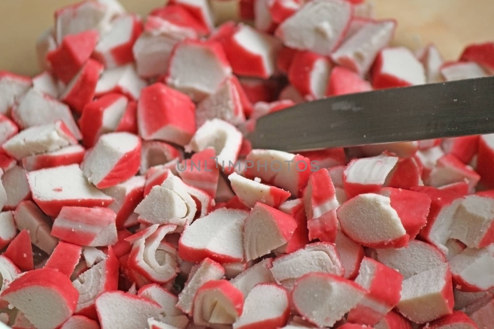 A whole plate of cutted crab sticks with a knife