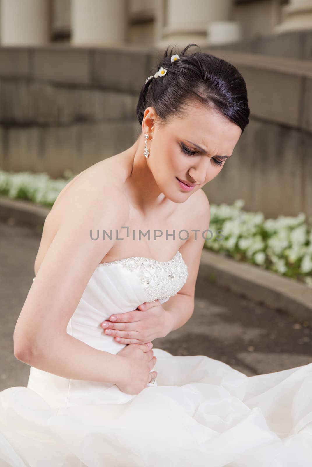 Bride with wedding dress sitting, having stomach ache
