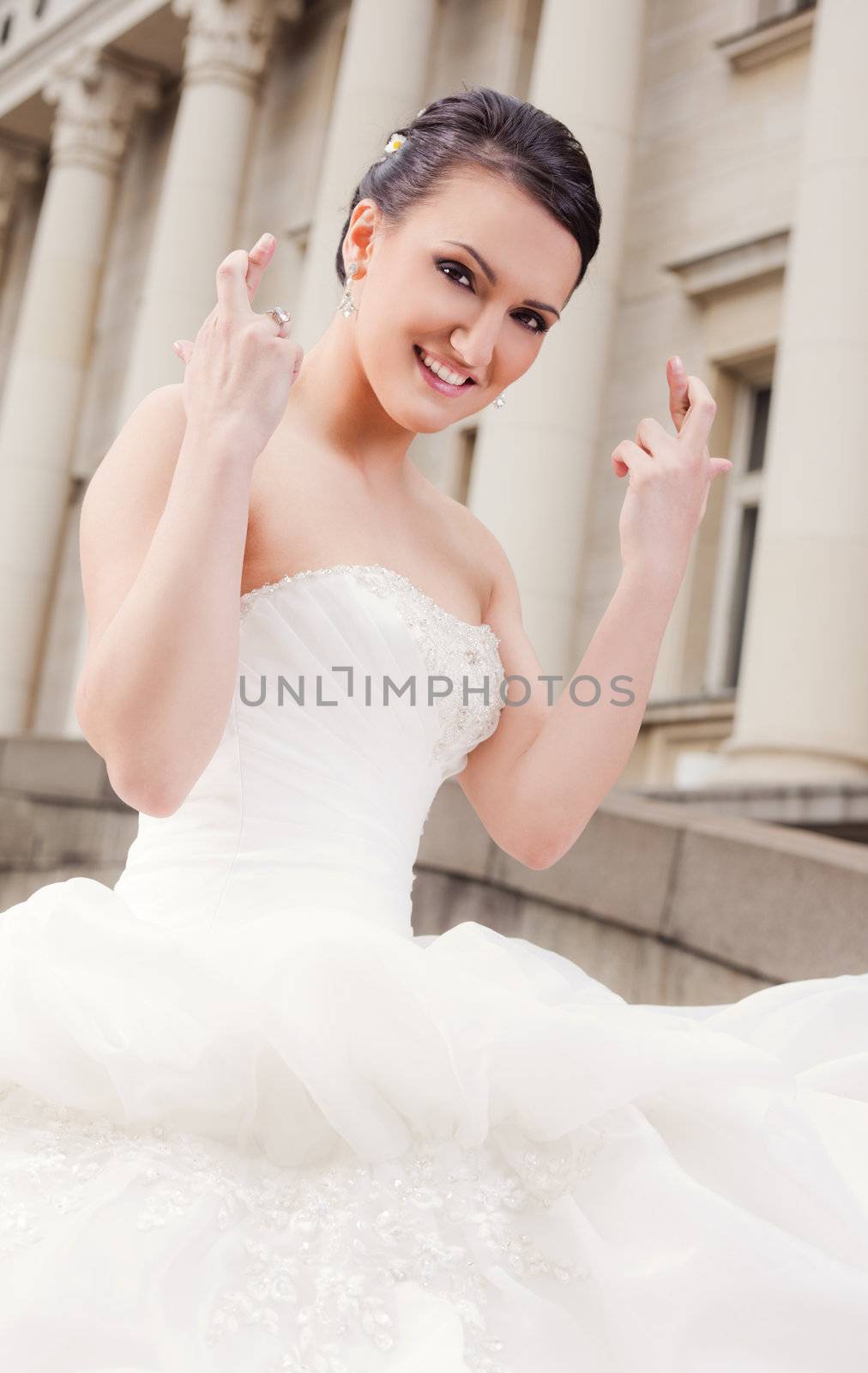 Happy bride with wedding dress showing fingers crossed