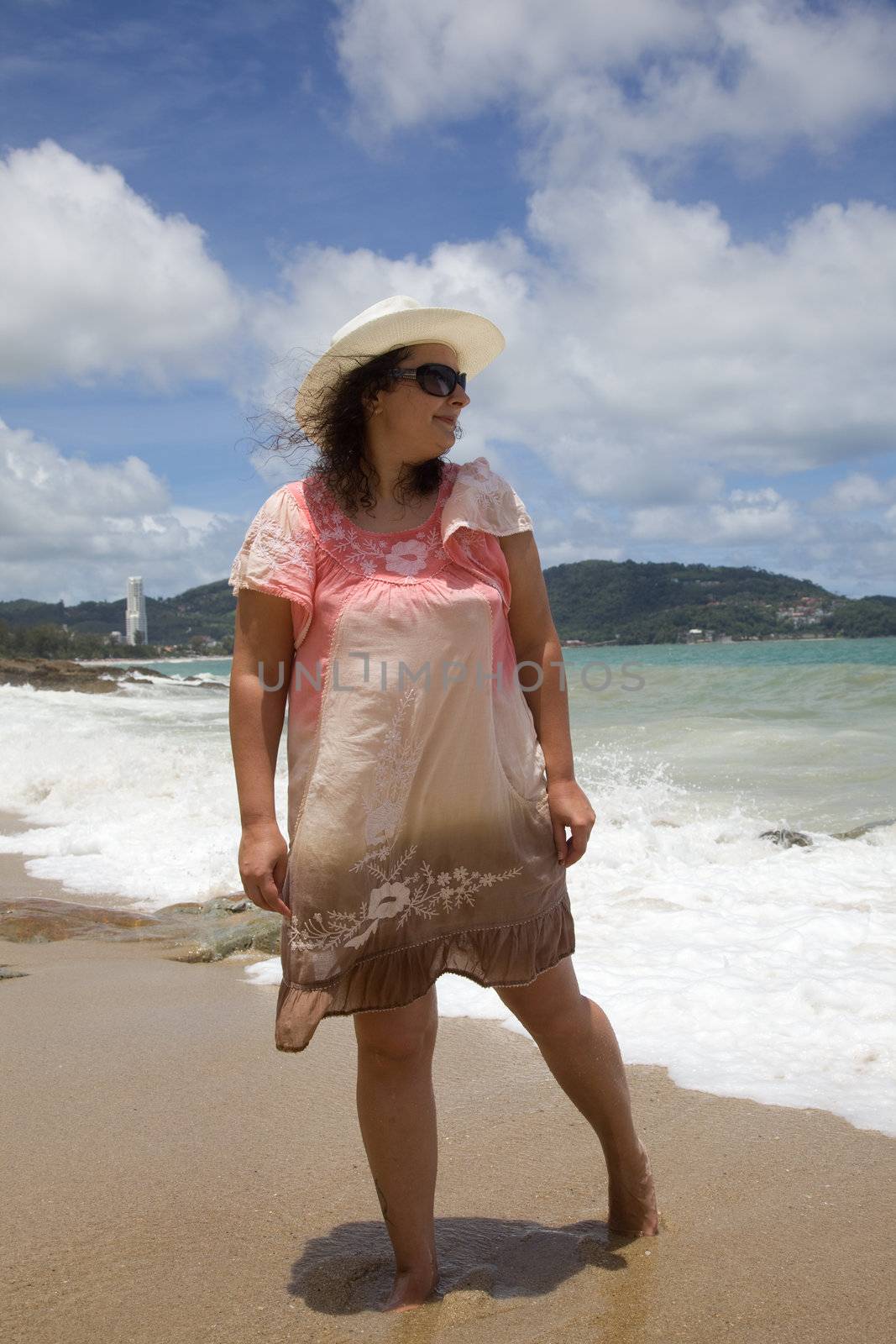 A woman in a white hat and a pink dress walking on the beach. Thailand.  Phuket