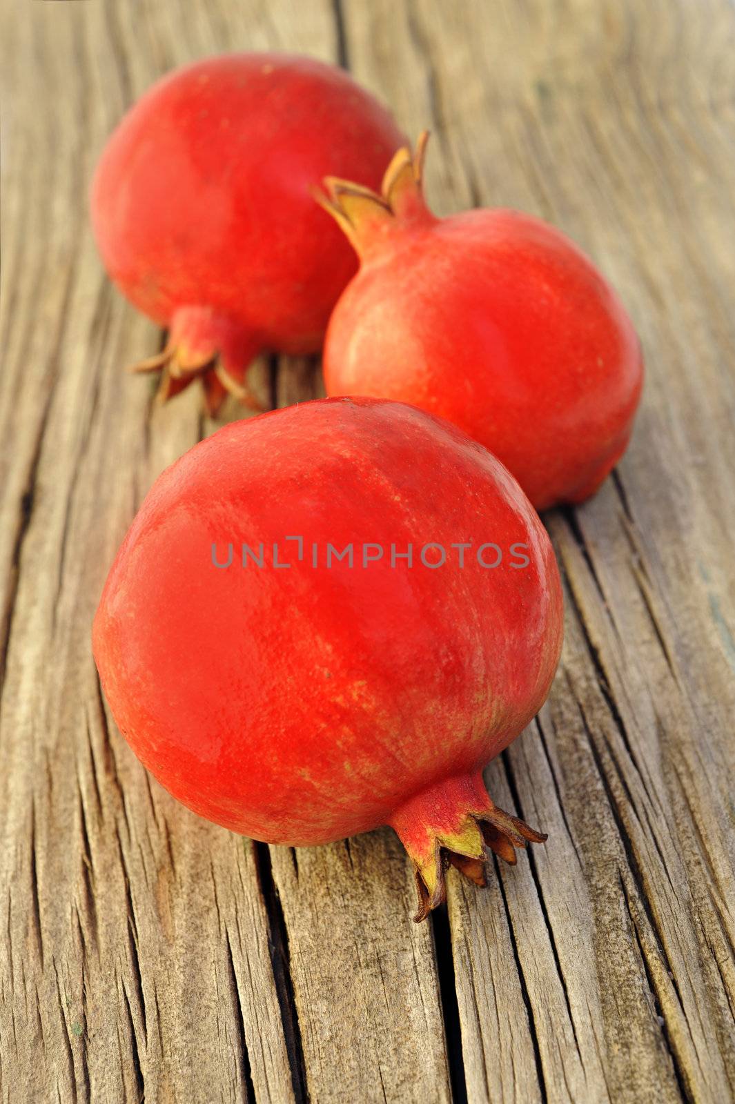 Three fresh red pomegranates on a wooden board by tish1