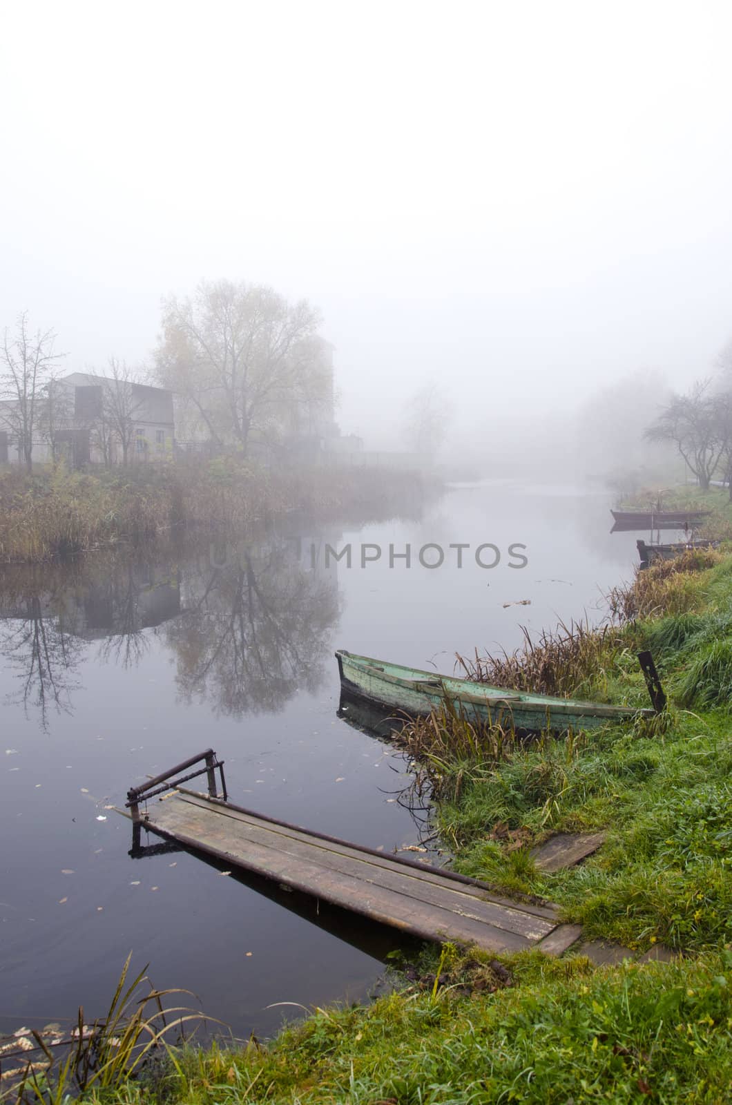 Wooden rowing boats and bridge standing on coast of river sunken in mysterious dence fog.