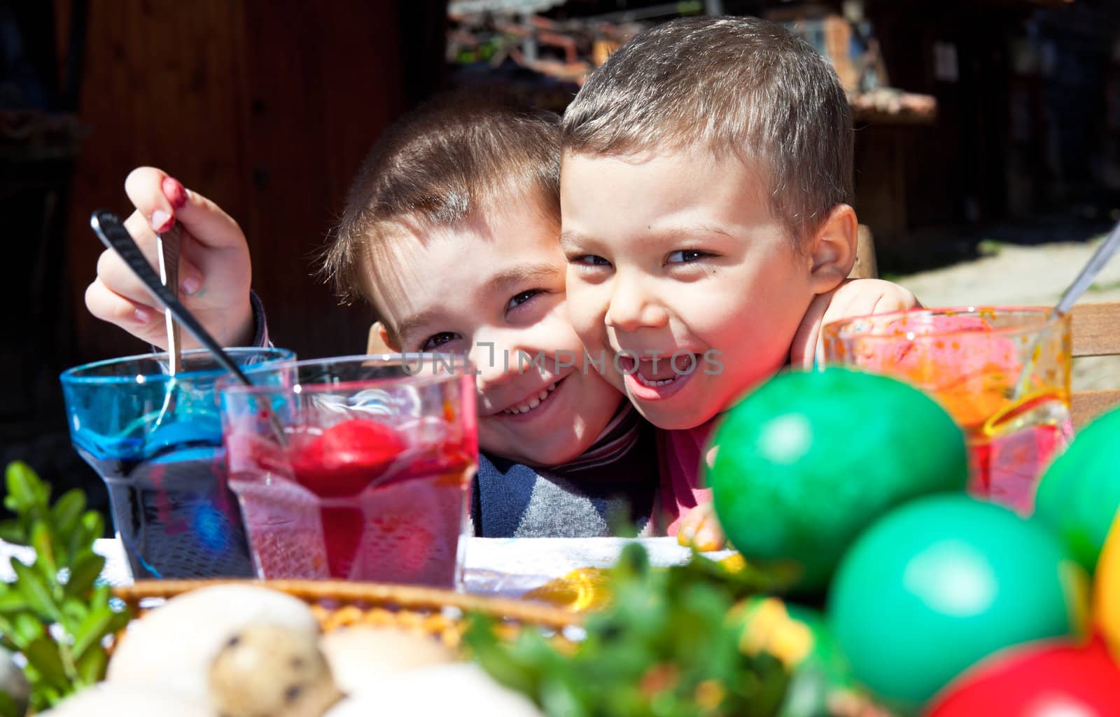 Two smiling little boys hugging and colouring easter eggs