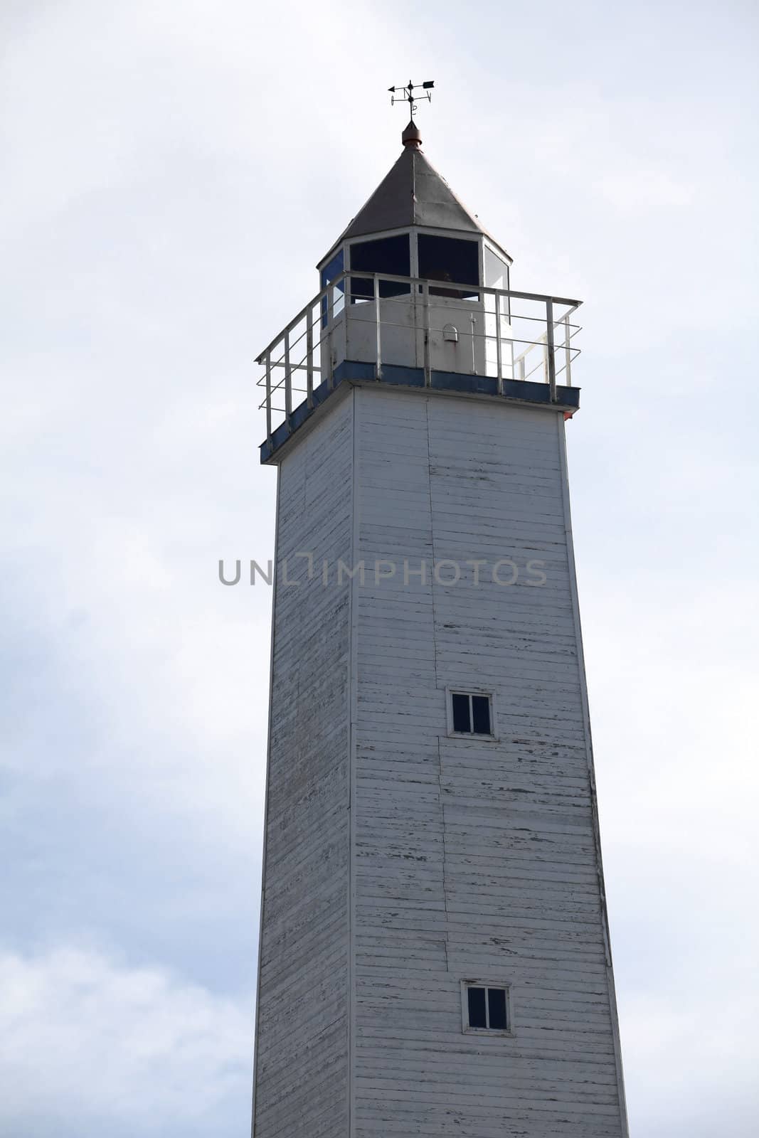 Old wooden lighthouse with an observation platform on the background of the cloudy sky