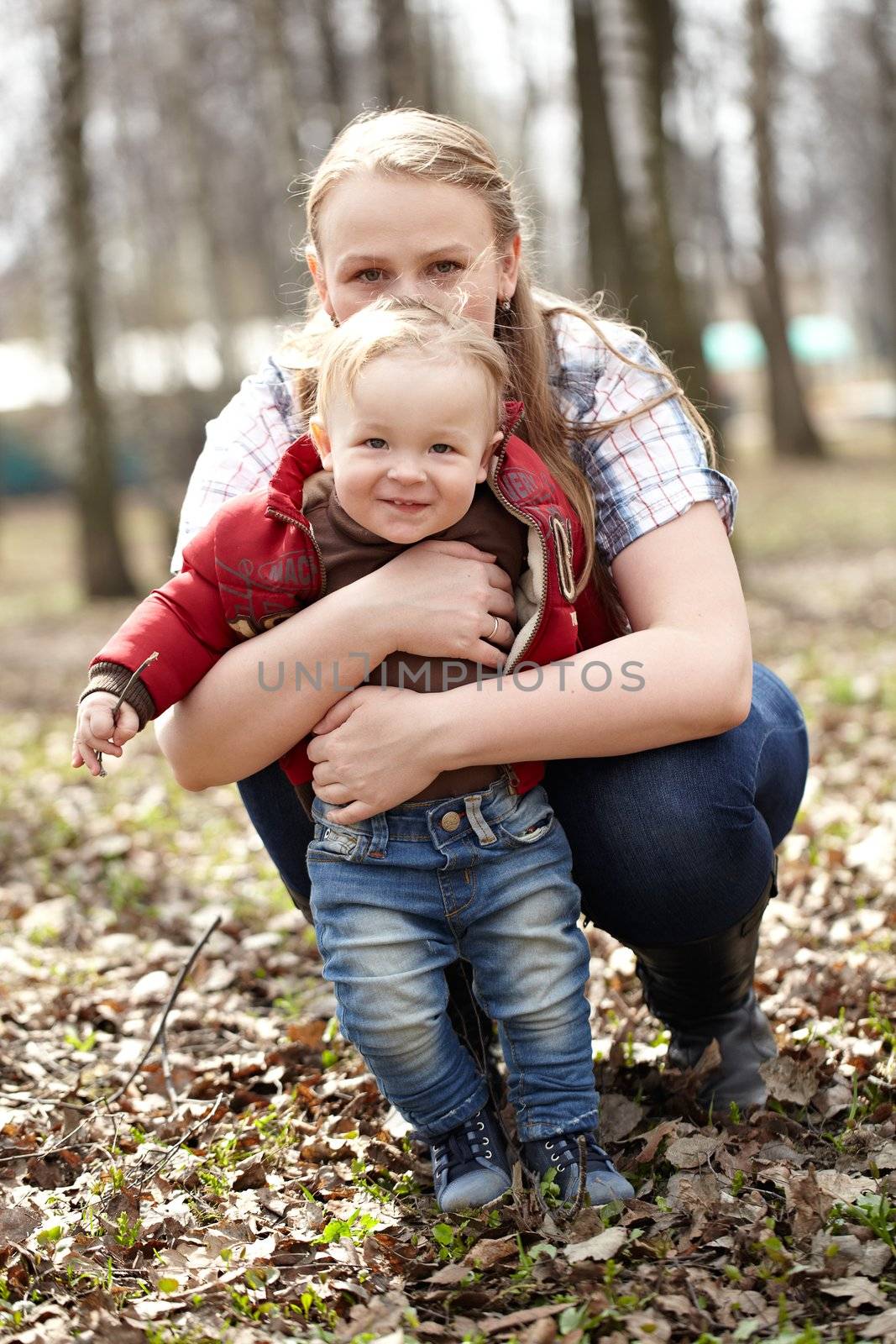 Beautiful young mother sitting behind her one year sonny and embracing him. This shot was made in the first day of spring.